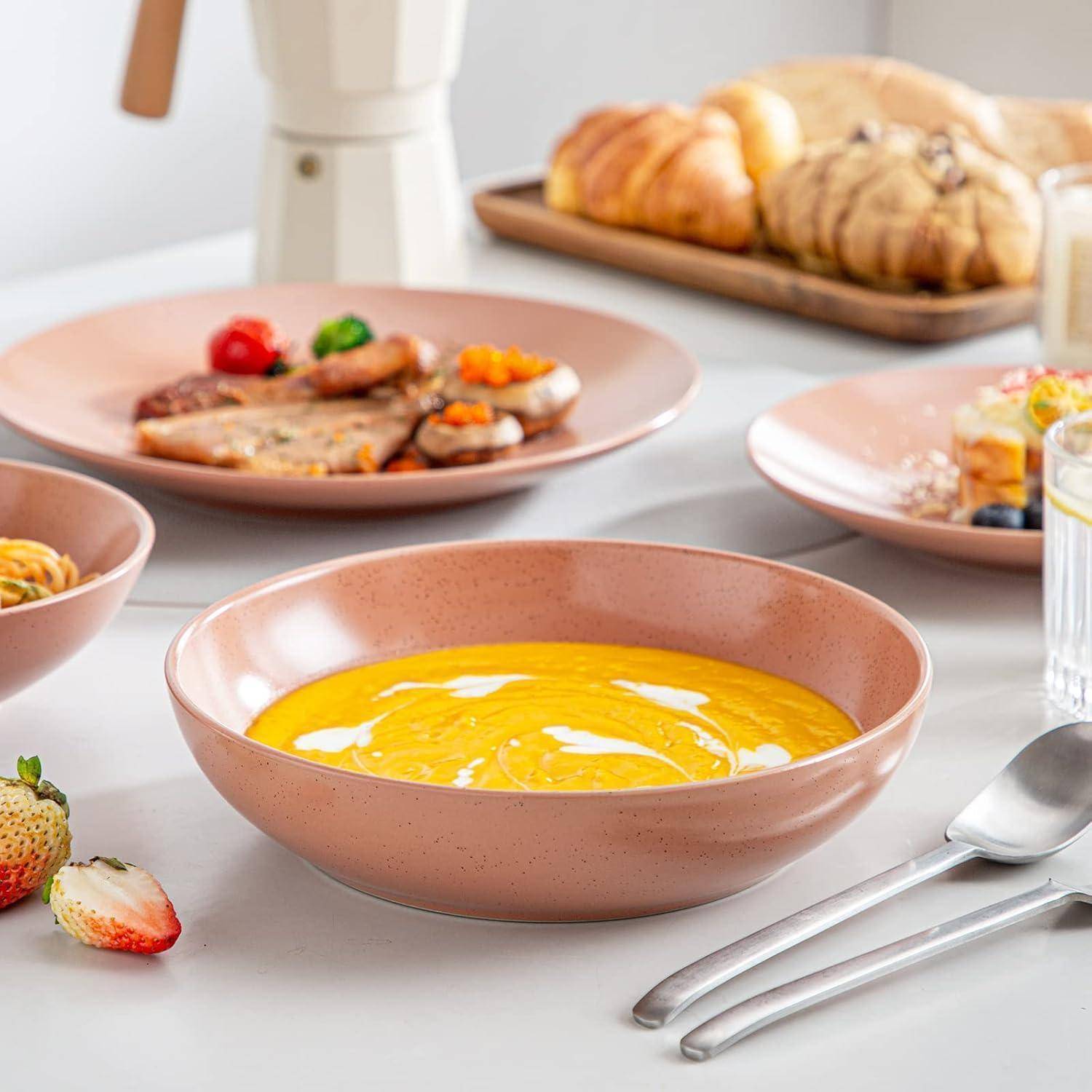 Eine Tischdecke mit einer Schüssel gelber Suppe, Tellern mit Speisen, Erdbeeren, Croissants und Besteck, was eine Frühstückssituation andeutet.