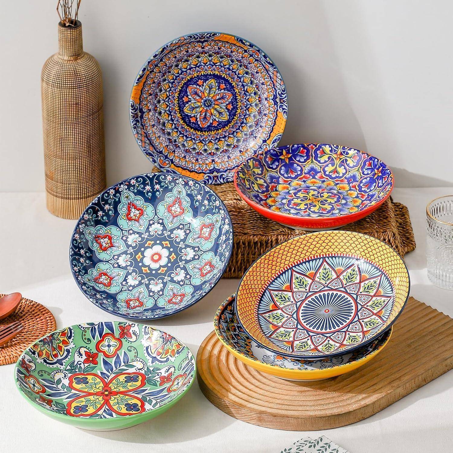 Bunte Keramikschüsseln mit kunstvollen Mustern auf einem Tisch, begleitet von einem geflochtenen Korb und einer dekorativen Vase im Hintergrund.