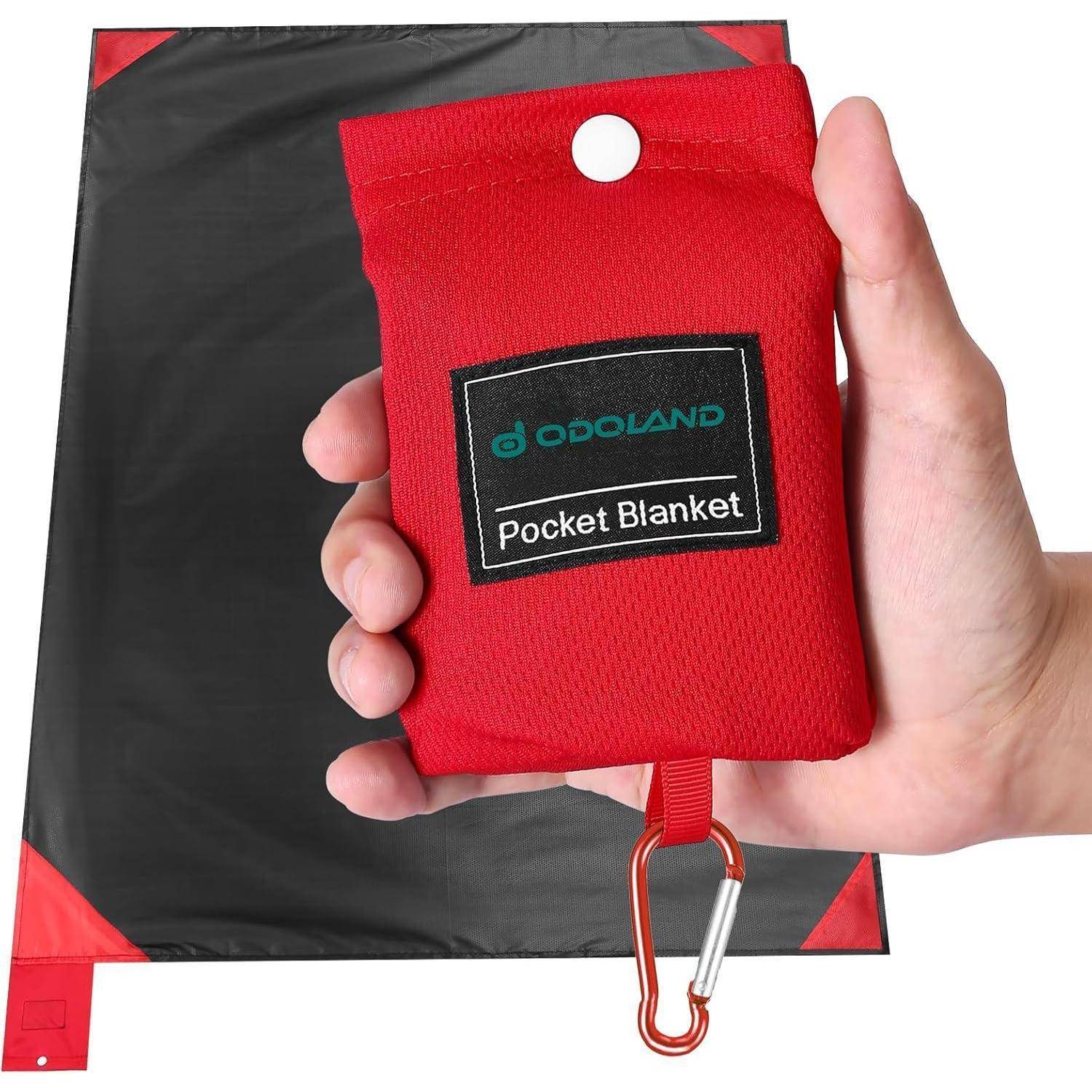 Hand hält einen roten Taschenbezug für eine Decke mit einem Karabiner; im Hintergrund eine ausgebreitete schwarze und rote Decke.