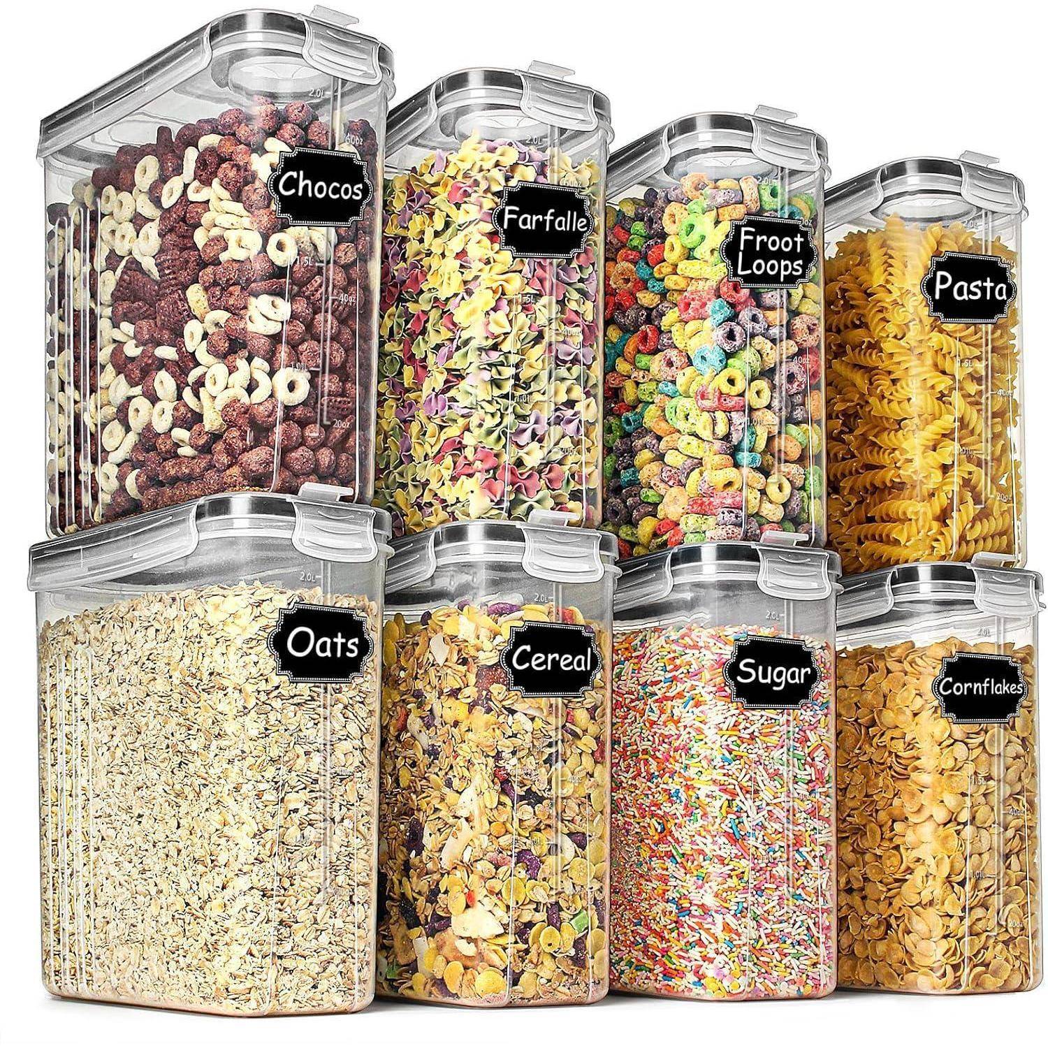 Acht durchsichtige Behälter gefüllt mit verschiedenen Trockenlebensmitteln, jeweils beschriftet: 'Chocos', 'Farfalle', 'Froot Loops', 'Pasta', 'Hafer', 'Müsli', 'Zucker', 'Cornflakes'.