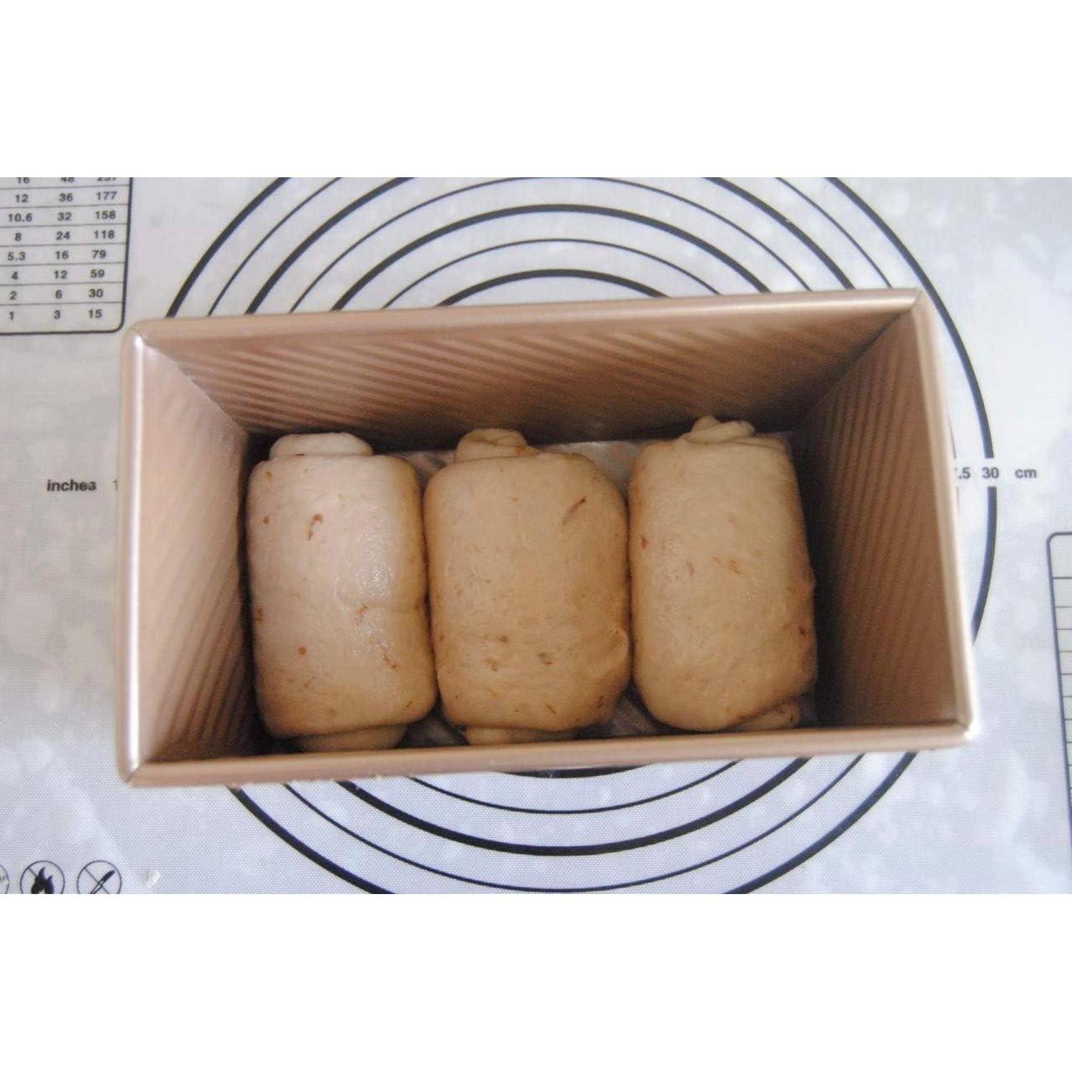 Teigrollen, gleichmäßig in einer rechteckigen Backform auf einer kreisförmig gemusterten Backunterlage angeordnet, bereit zum Backen.