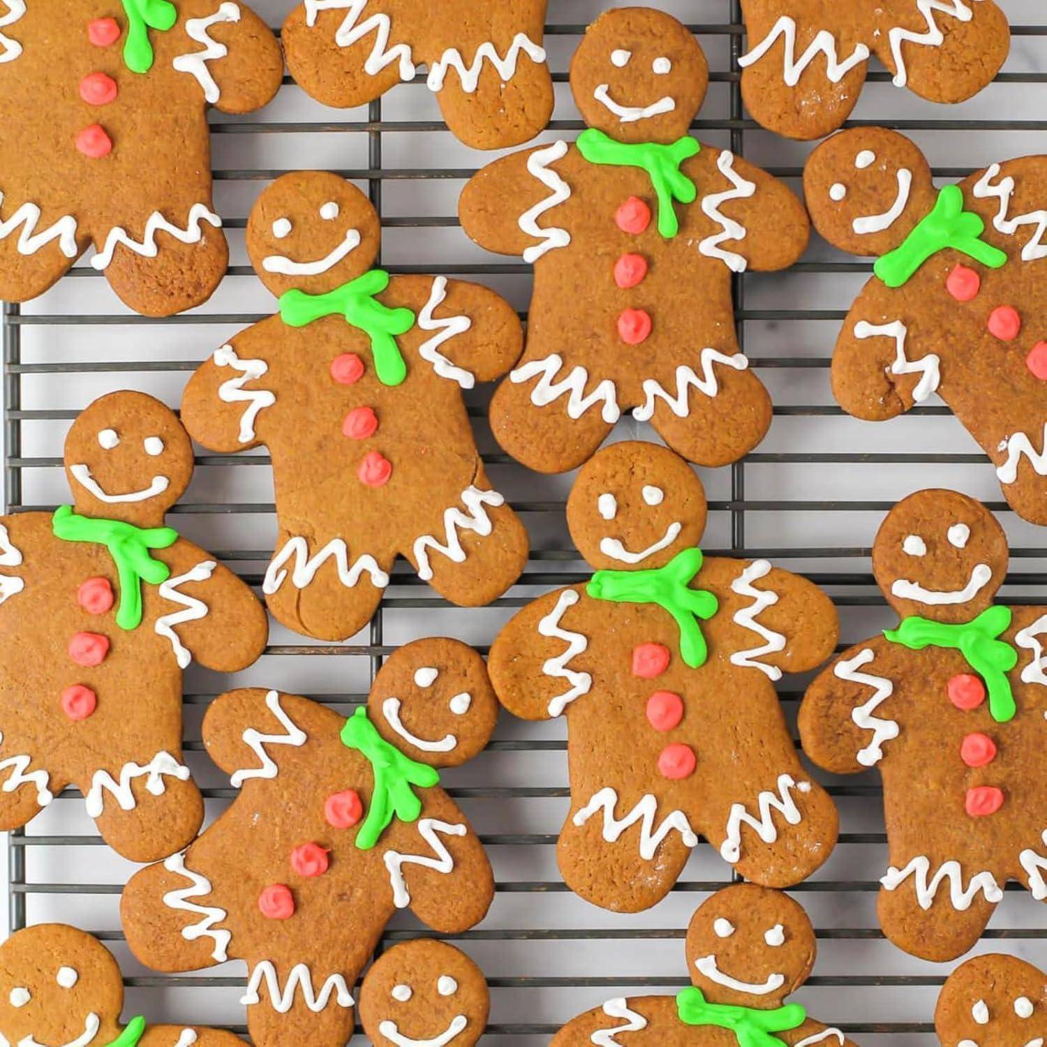 Lebkuchenmännchen, die mit Zuckerguss für Augen, Münder, Knöpfe und grüne Schals verziert sind, auf einem Kuchengitter angeordnet.
