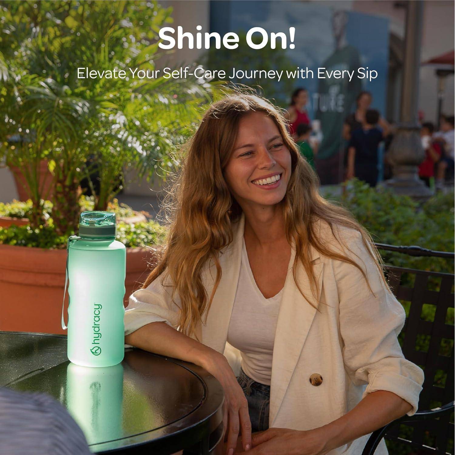 Eine Frau, die an einem Tisch sitzt, lächelt neben einer Wasserflasche mit dem Logo 