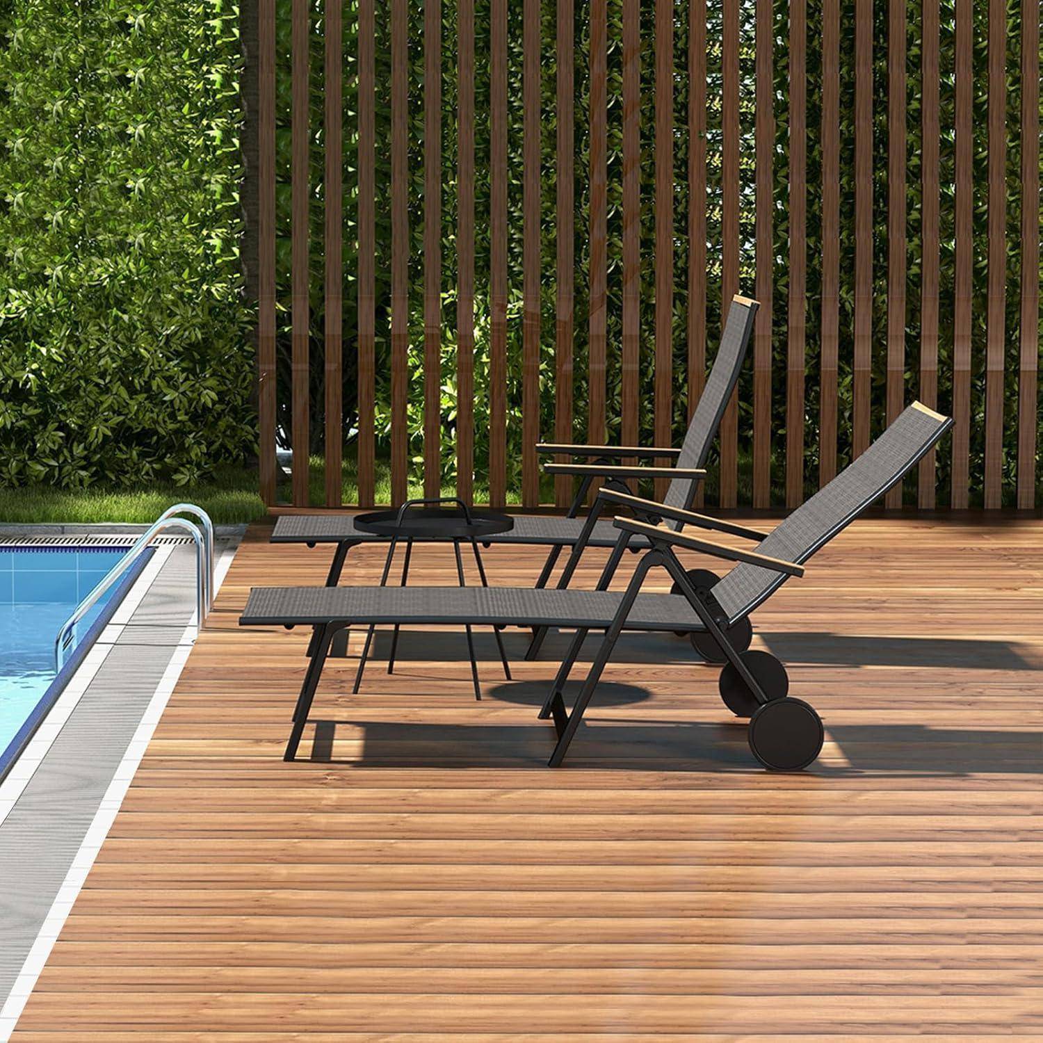 Zwei Liegestühle und ein kleiner Tisch auf einer Holzterrasse neben einem Pool, mit einem vertikalen Holzlattenzaun und Grünpflanzen im Hintergrund.