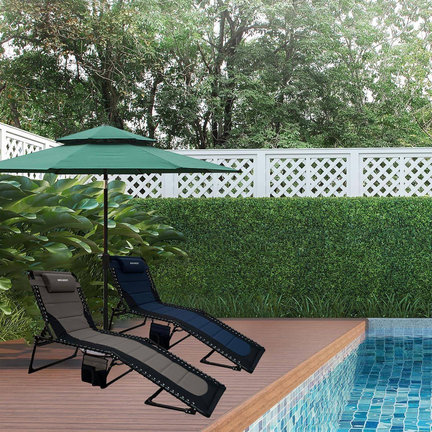 Zwei Liegestühle mit Sonnenschirmen stehen auf einer Holzterrasse neben einem Swimmingpool, umgeben von üppiger Vegetation und einem Rankzaun.