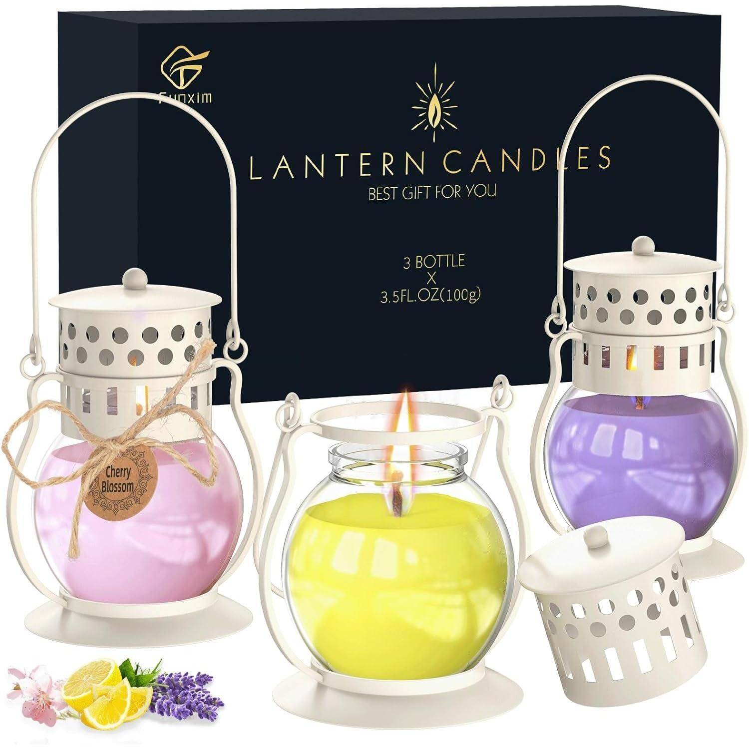 Ein Set aus drei Kerzen in weißen Laternenhaltern mit farbigem Wachs: lila, gelb und lavendel. Inklusive einer dekorativen schwarzen Geschenkbox.