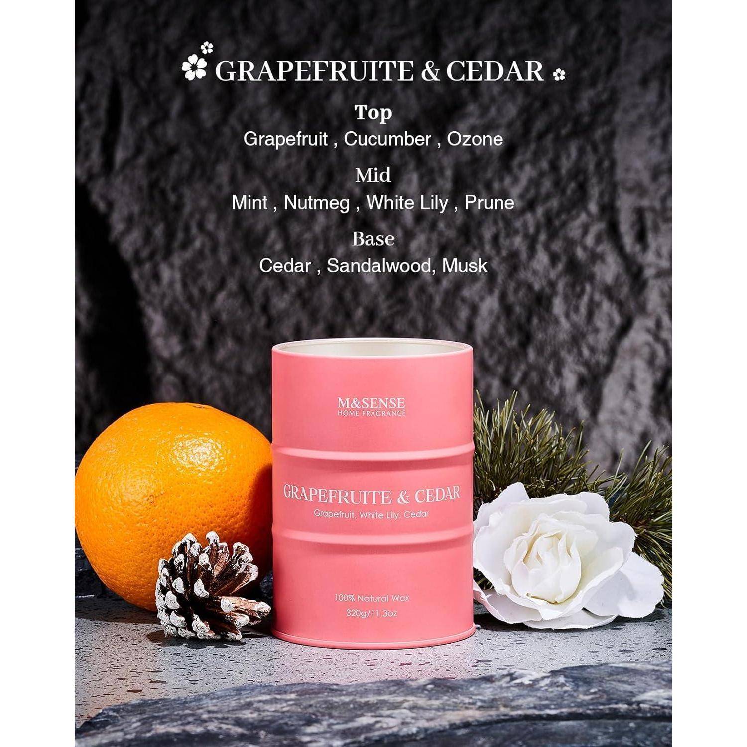Eine Kerze mit rosa Grapefruit und Zeder steht auf einer Steinoberfläche, dekoriert mit einer Grapefruit, einem Tannenzapfen und einer weißen Blume. Der Text listet die Duft-Kopf-, Herz- und Basisnoten auf.