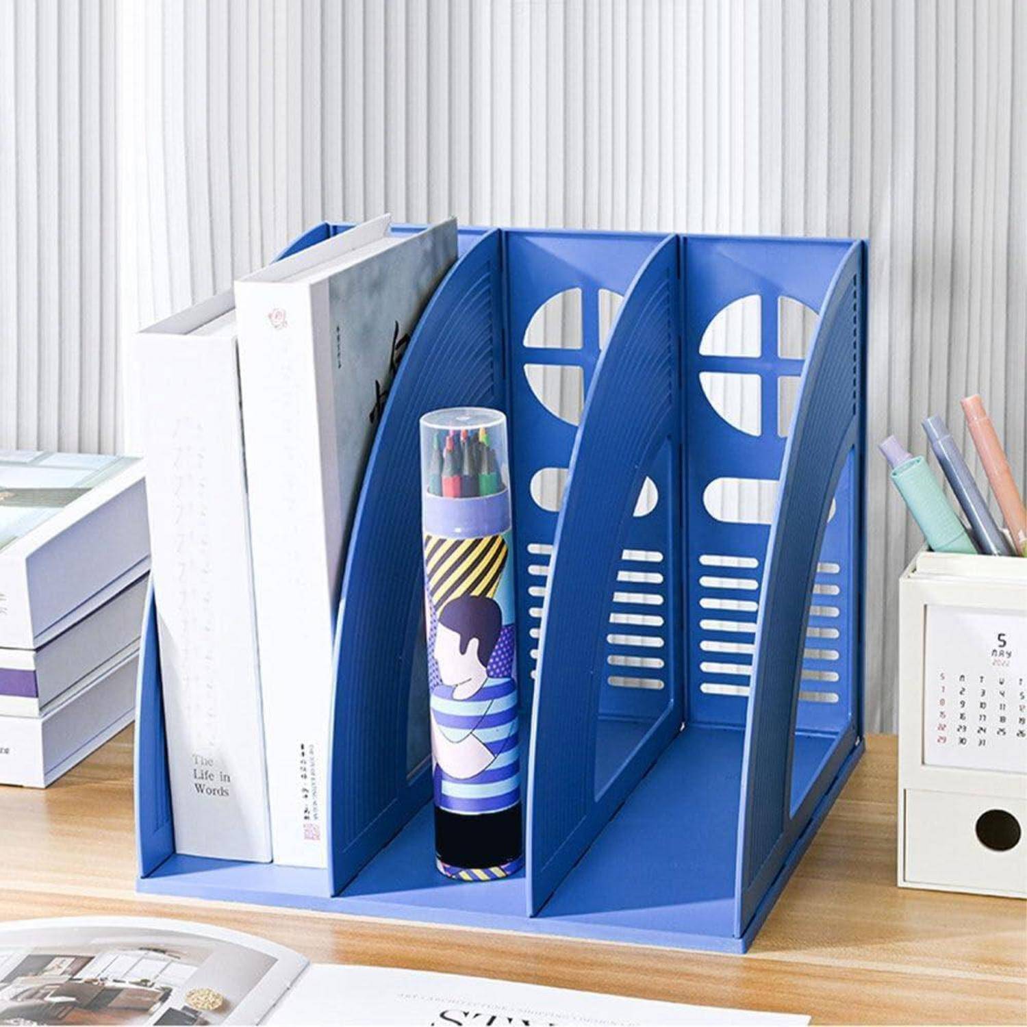 Blauer Schreibtischorganizer hält einige Bücher und einen Stiftehalter mit Markern, platziert auf einem Holzschreibtisch mit zusätzlichen Büromaterialien.