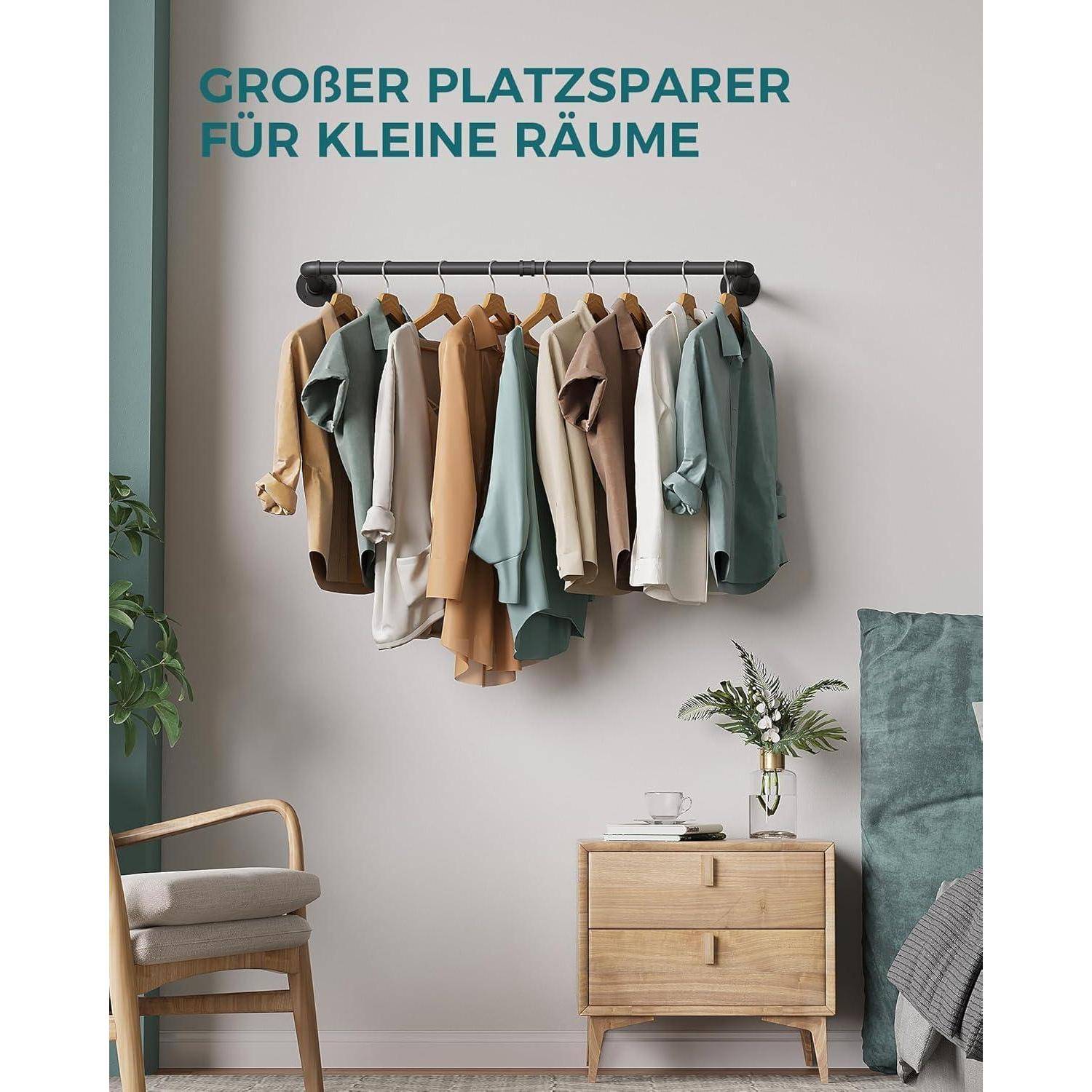 Ein kompaktes Kleidungsständer mit Hemden und Jacken ist an einer Wand montiert. Darunter steht ein Holznachttisch mit einer Blumenvase neben einem Stuhl.