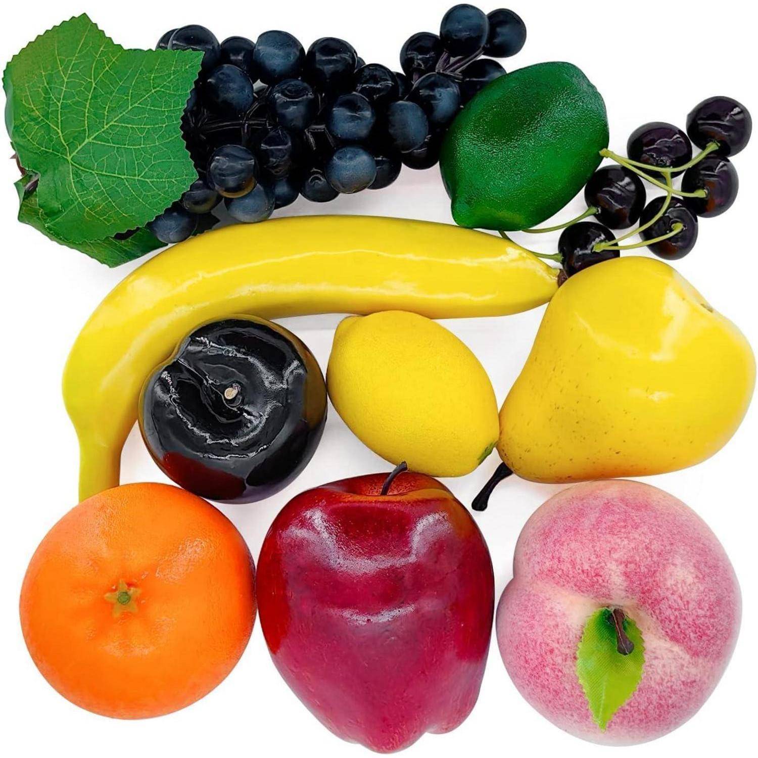 Eine Ansammlung künstlicher Früchte, darunter Trauben, Banane, Zitrone, Pflaume, Apfel, Pfirsich und Mandarine, angeordnet auf einem weißen Hintergrund.