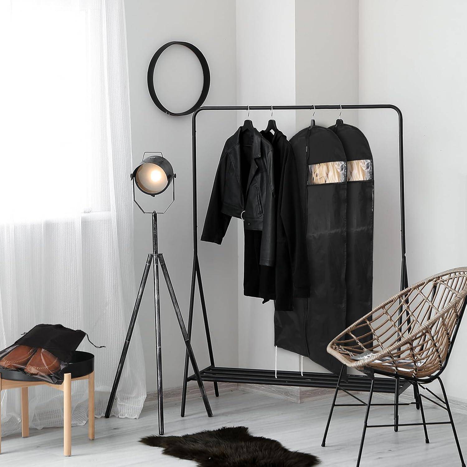 Ein minimalistisches Zimmer mit einer Kleiderstange, an der schwarze Kleidungsstücke hängen, einem Scheinwerfer, einem Drahtsessel und durchsichtigen Vorhängen, die natürliches Licht filtern.
