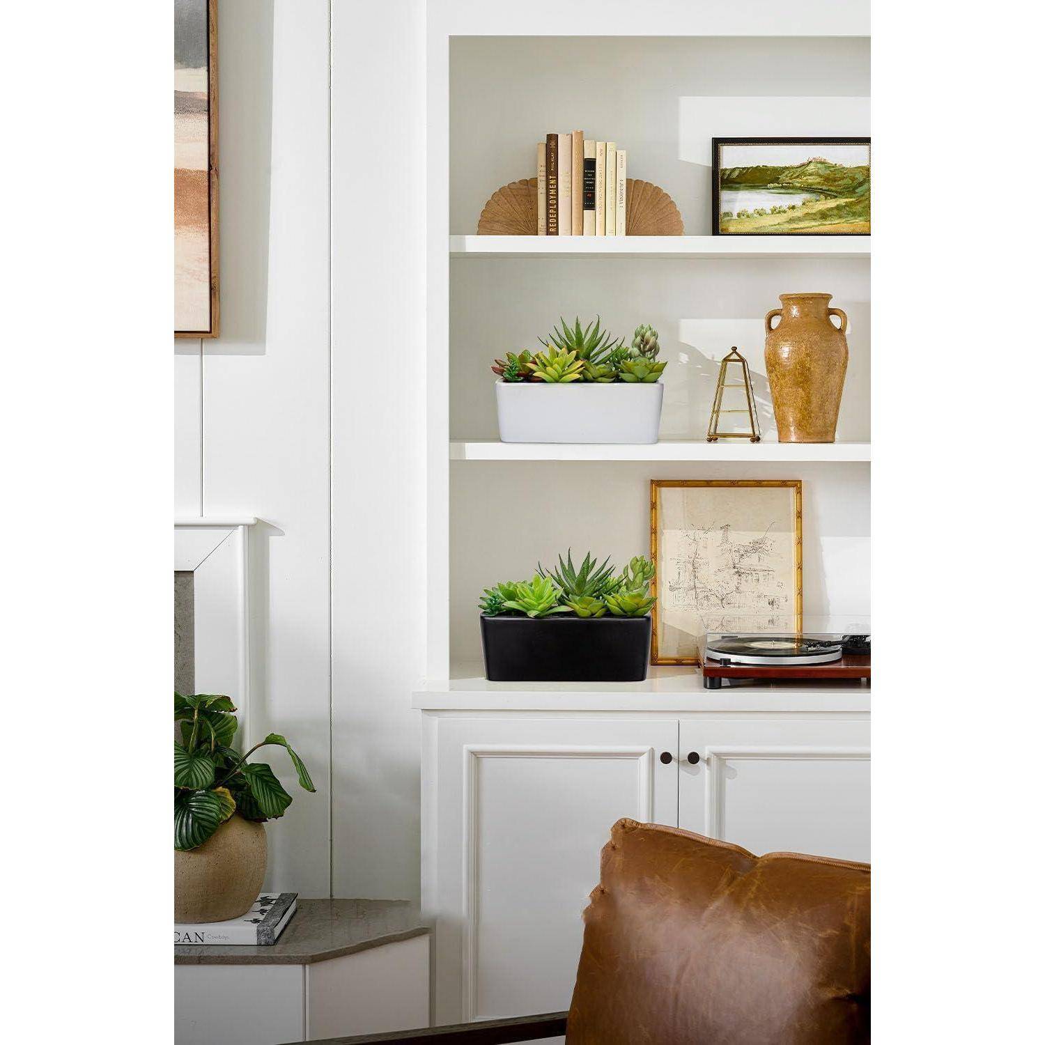 Bücherregal mit dekorativen Gegenständen wie Büchern, Pflanzen, Töpfereien und einem Plattenspieler. Weiße Regale und Wand schaffen einen minimalistischen Look.