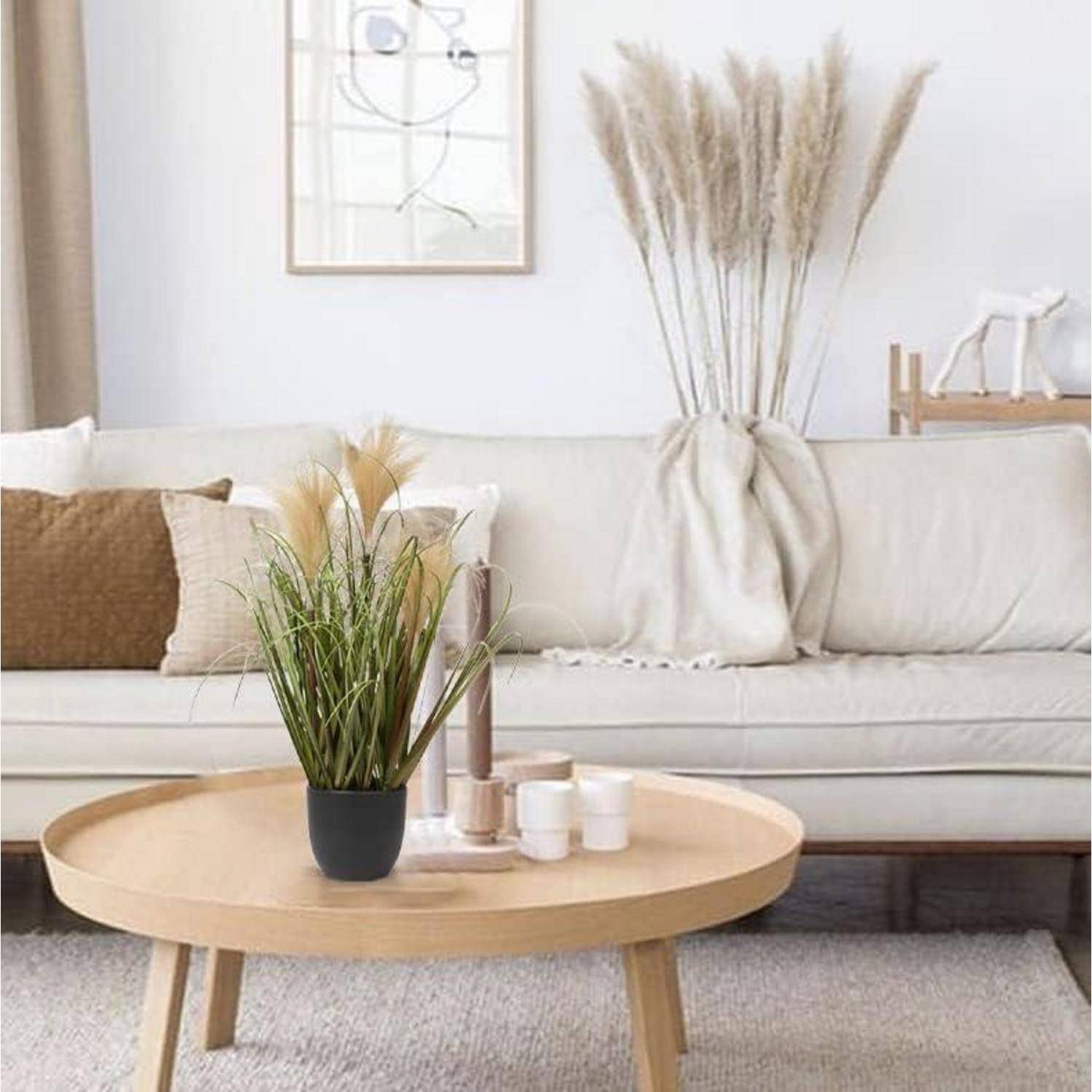 Ein gemütliches Wohnzimmer mit einem Sofa in neutralen Tönen, einem runden Holzkaffeetisch mit dekorativen Pflanzen, Pampasgras und minimalistischer Wandkunst.