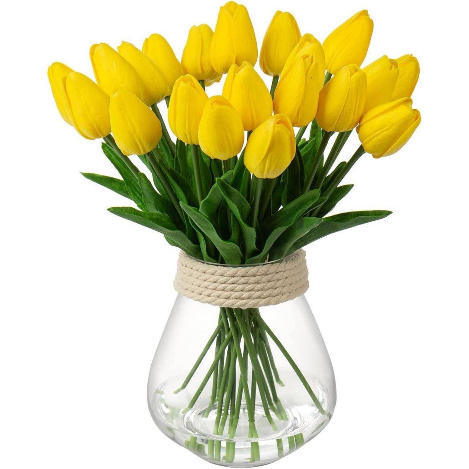 Eine klare Glasvase enthält einen Blumenstrauß aus leuchtend gelben Tulpen mit grünen Stängeln, in einer vollständigen, symmetrischen Anordnung.
