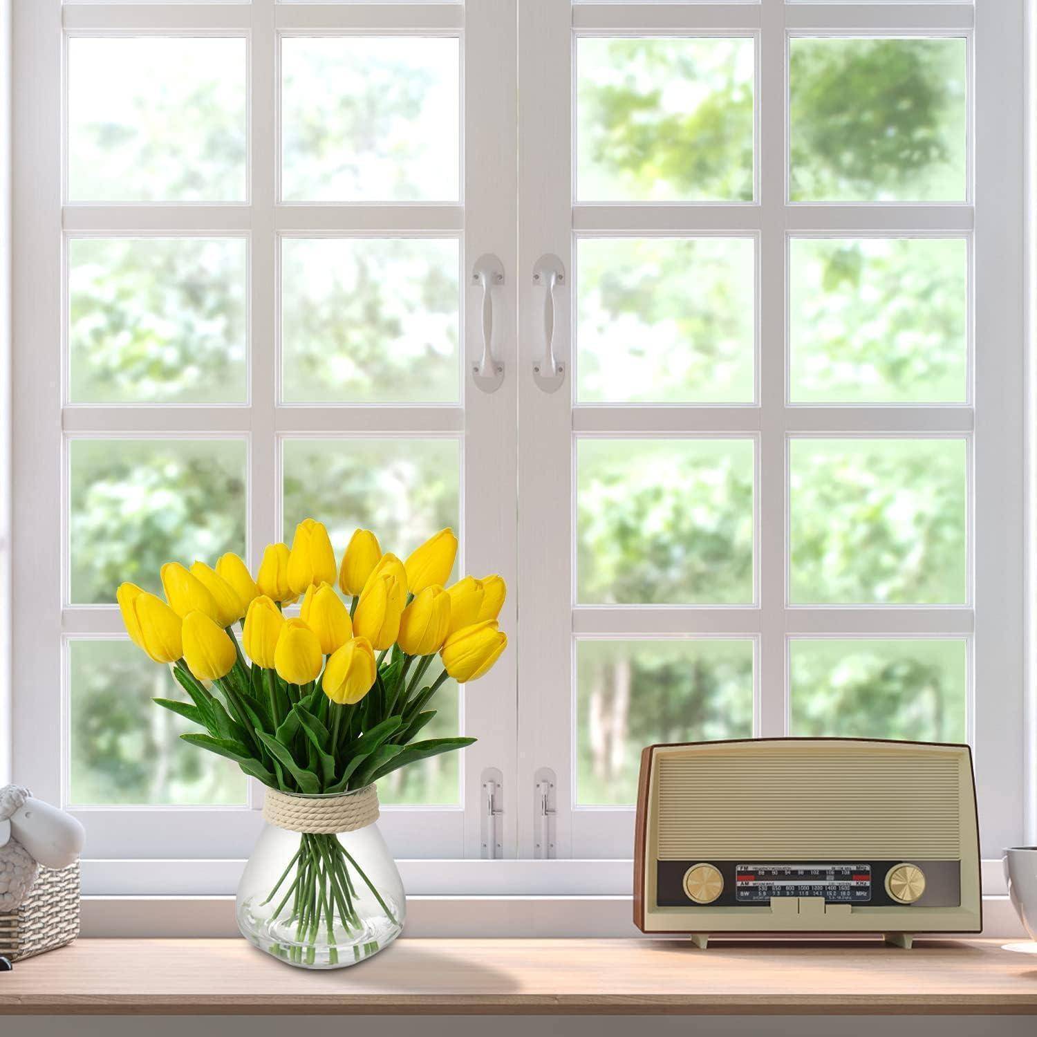 Eine Vase mit gelben Tulpen steht auf der Fensterbank neben einem Vintage-Radio. Das Fenster zeigt einen klaren, hellen Tag draußen.