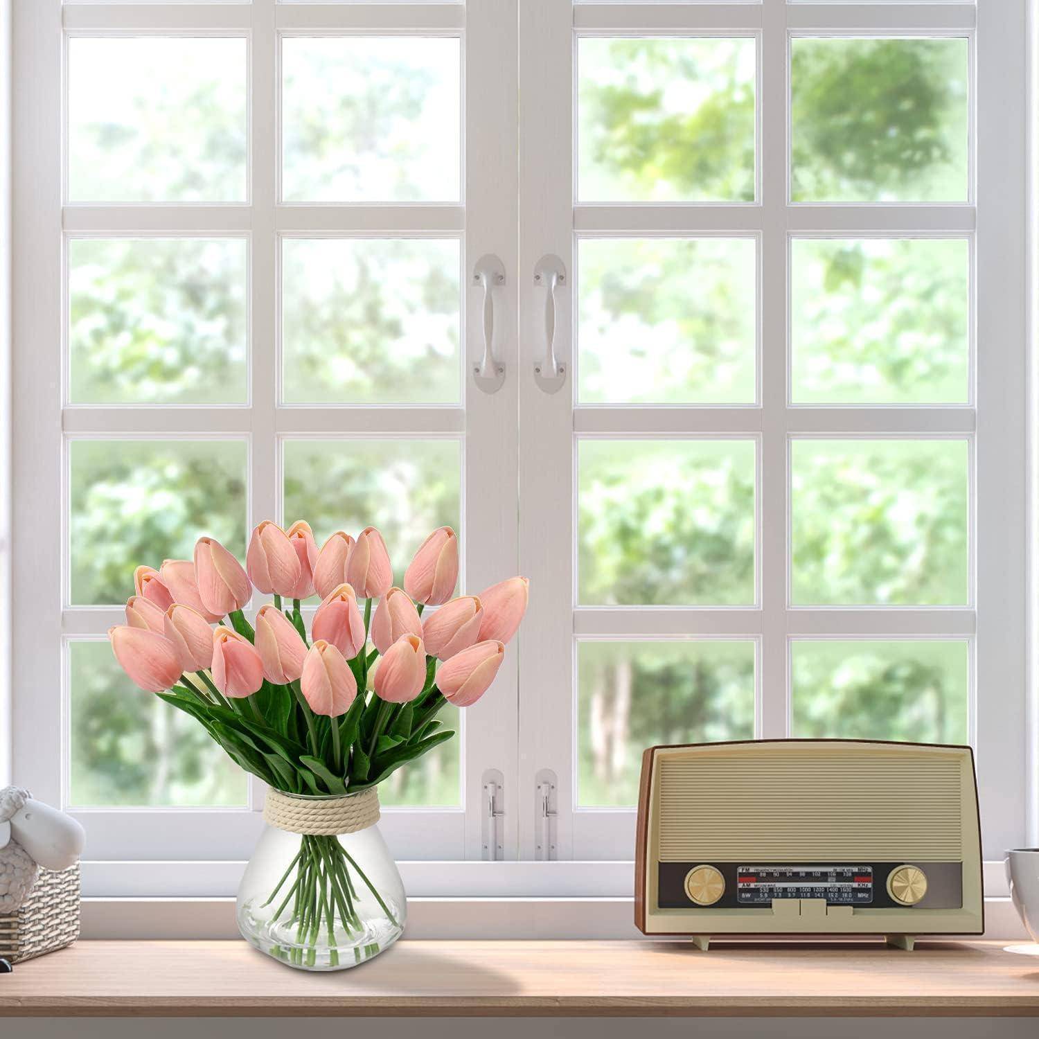 Eine Vase mit pinken Tulpen und ein Retroradio auf einer Fensterbank, mit Blick durchs Fenster auf grünes Blattwerk draußen.