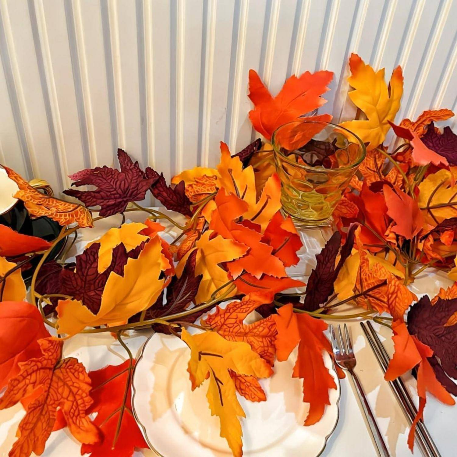 Herbstlich gestaltete Tischdecke mit bunten Herbstblättern, die um weiße Teller und Besteck verstreut sind und eine festliche, saisonale Atmosphäre schaffen.