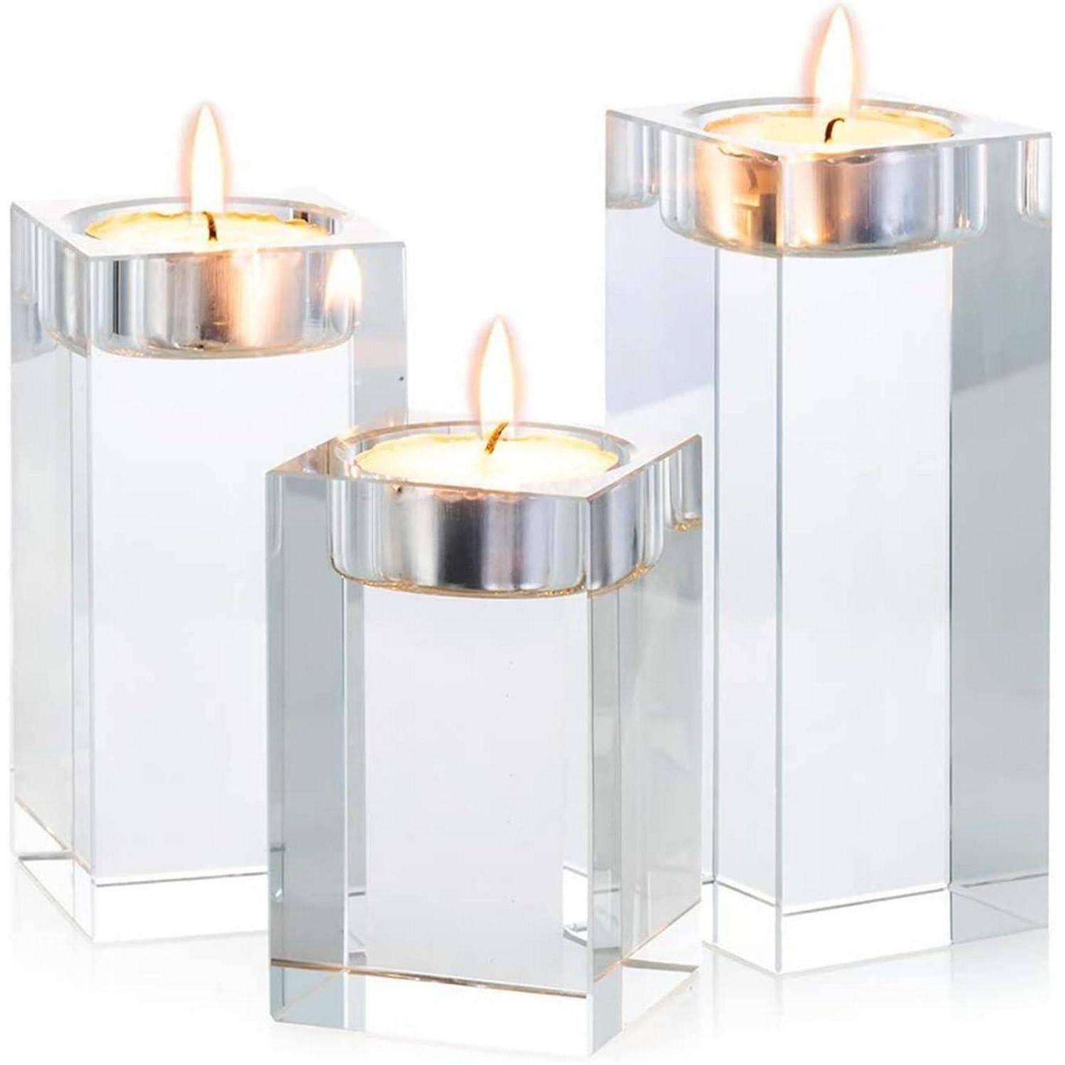 Drei Kerzenhalter aus Glas in unterschiedlichen Höhen, jeweils mit einer brennenden Teelichterkerze, zusammen auf einem schlichten Hintergrund platziert.