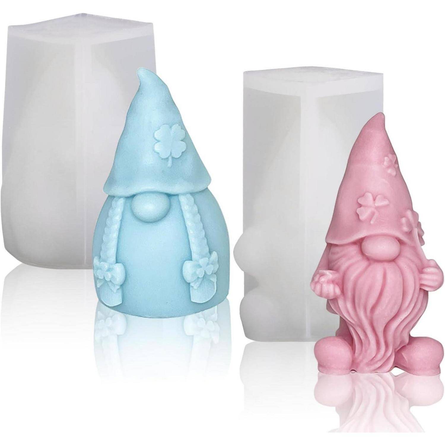 Zwei gnomartige Kerzen, eine blaue mit Zöpfen und einem Hut und eine rosa mit Bart und Hut, werden zusammen mit ihren Gussformen präsentiert.
