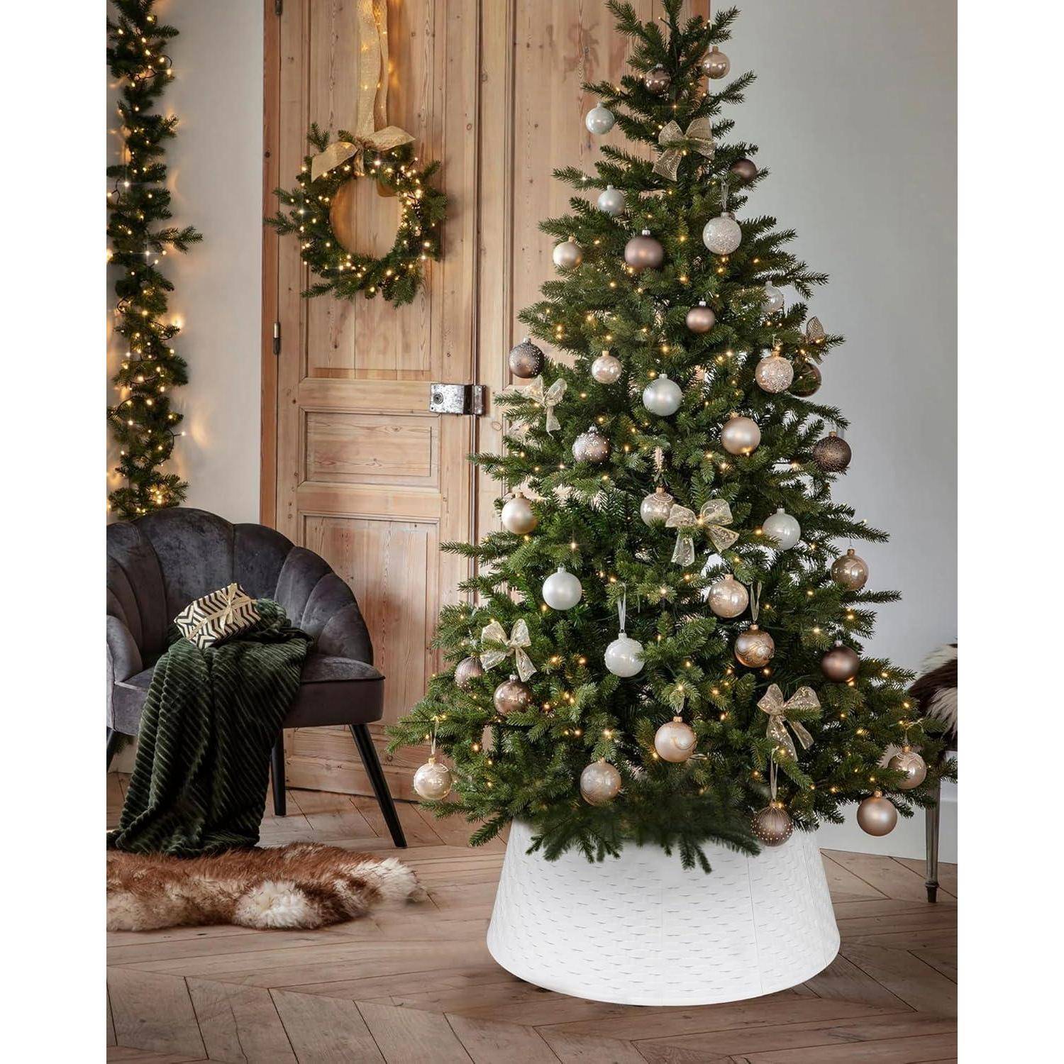 Ein geschmückter Weihnachtsbaum mit gold- und silberfarbenen Schmuckstücken steht in einem gemütlichen Wohnzimmer. Ein grüner Kranz hängt an einer Holztür in der Nähe.