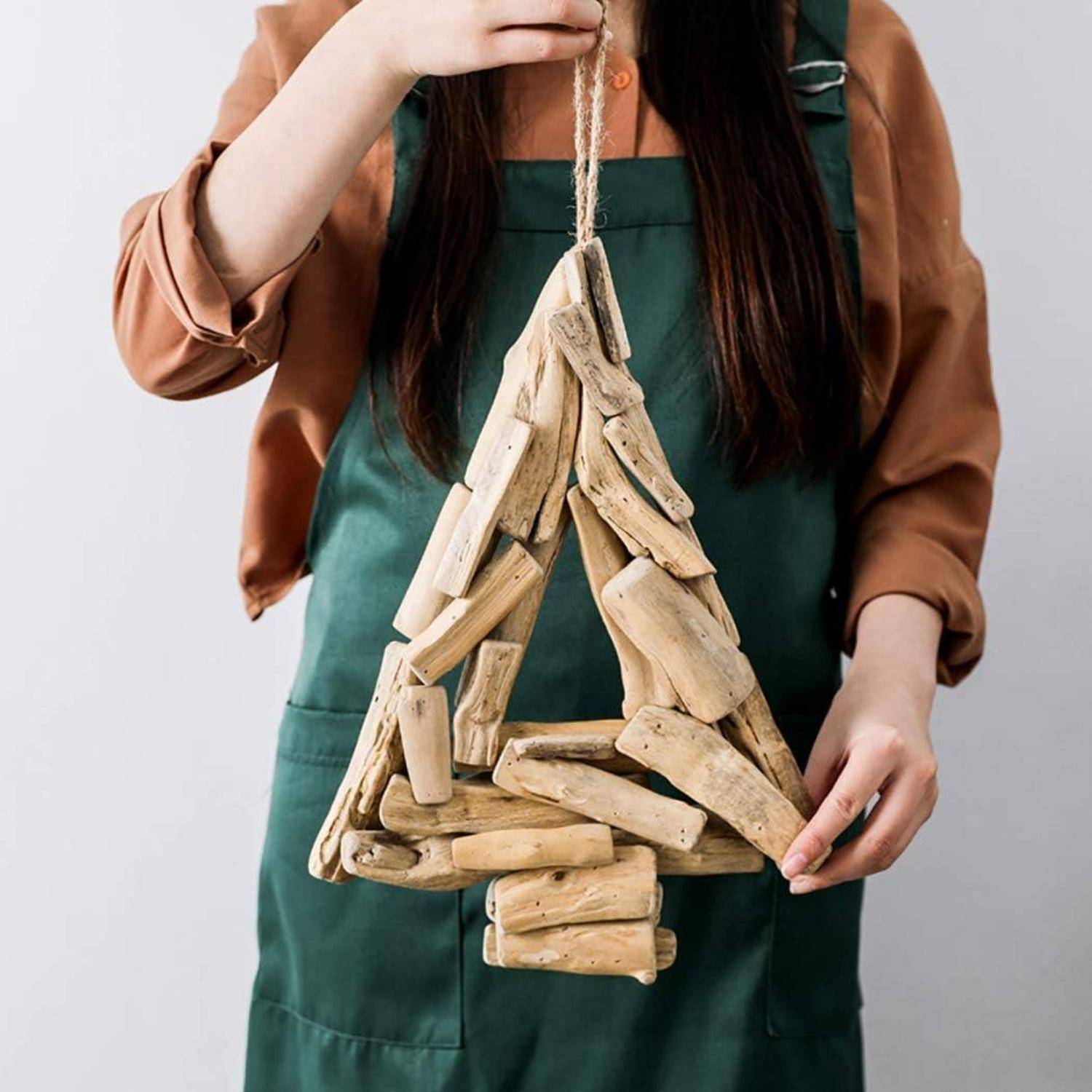 Eine Person in einer grünen Schürze hält eine Weihnachtsbaumdekoration aus Holzstäben, die zu einer dreieckigen Form zusammengesetzt ist.