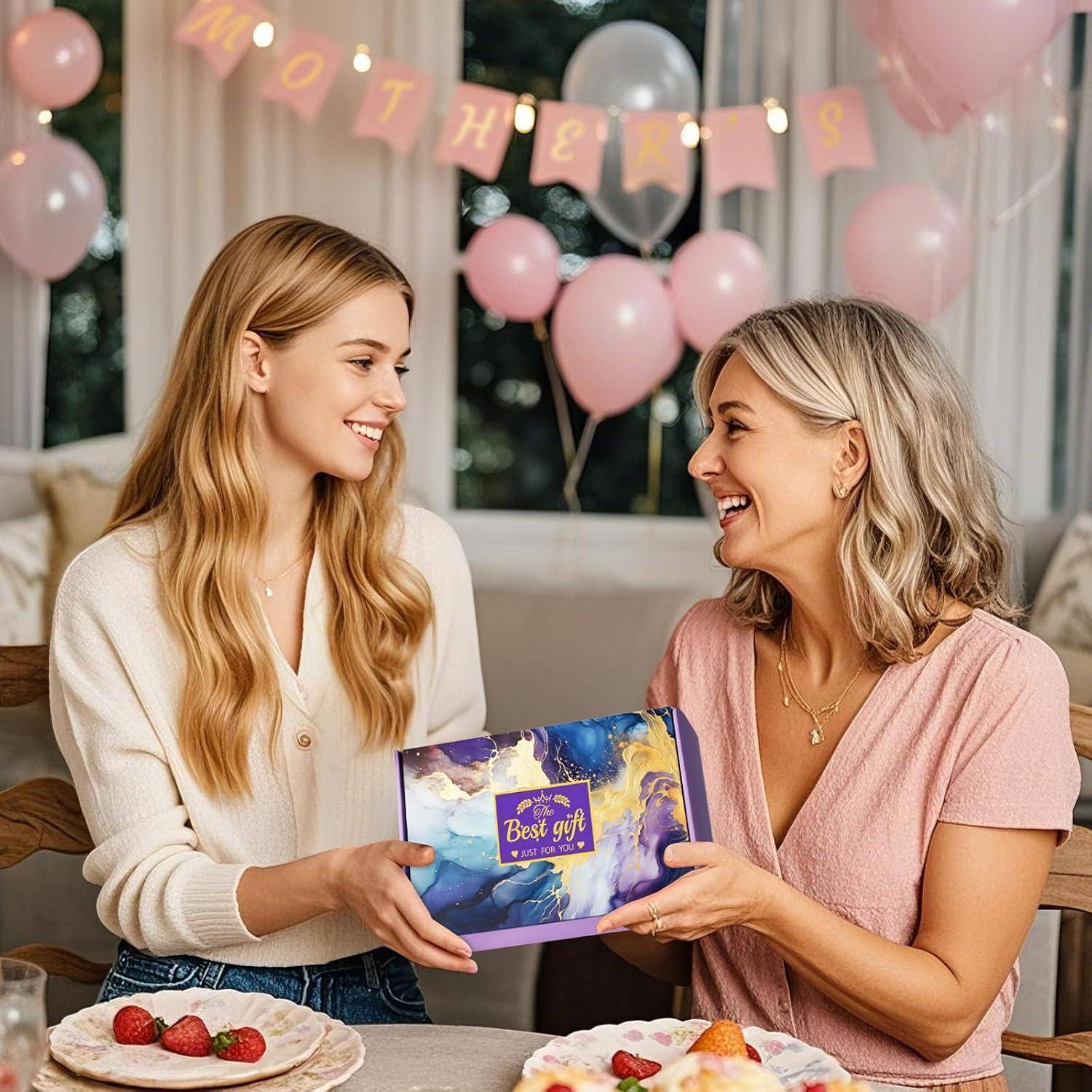 Zwei lächelnde Frauen sitzen an einem Tisch mit Tellern voller Speisen und halten eine Geschenkbox mit der Aufschrift 