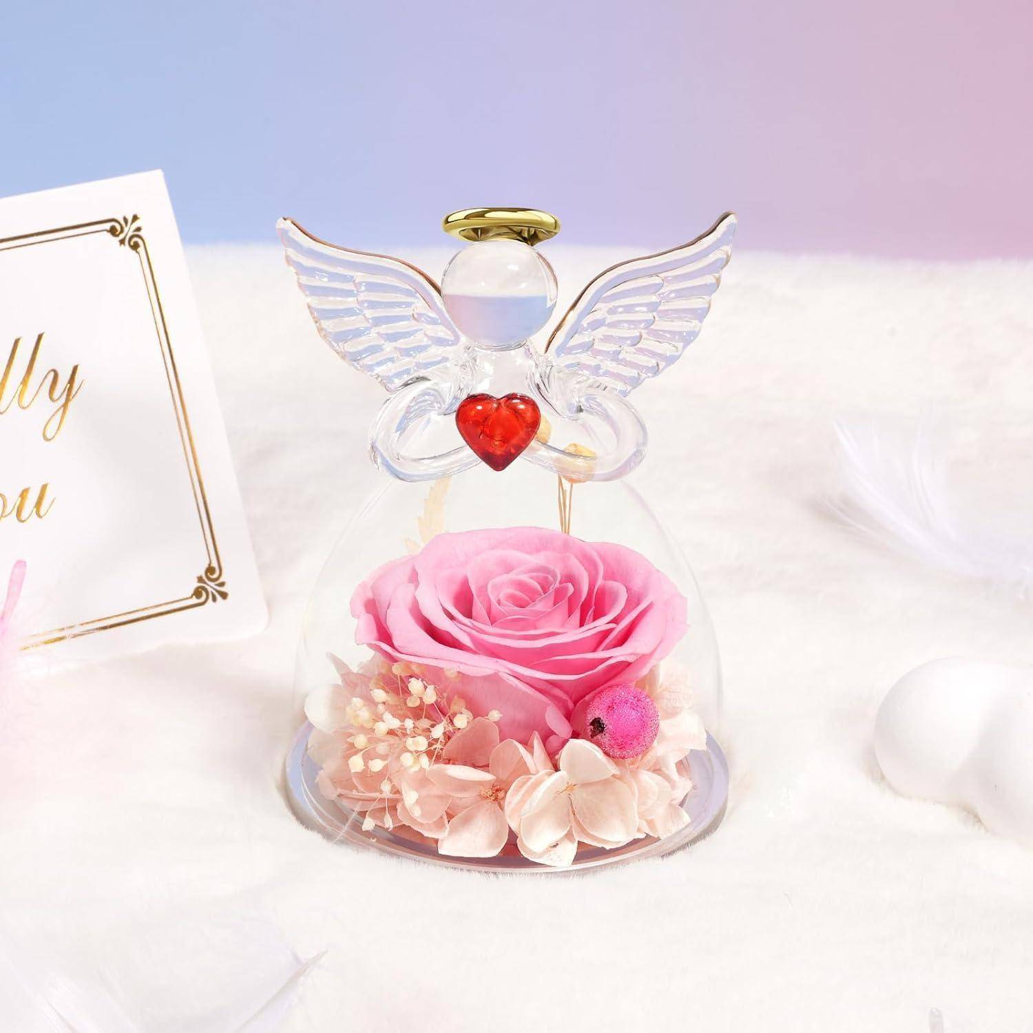 Eine Engelsfigur mit einem Herzen und transparenten Flügeln umschließt eine rosa Rose und Blumen. Eine Karte ist zu sehen mit Schreibschrifttext.