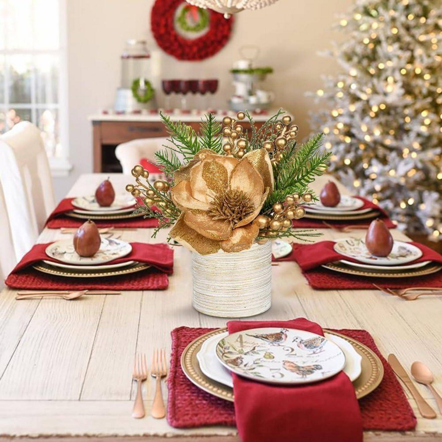 Ein festlich gedeckter Weihnachtstisch mit roten Servietten, kunstvollen Tellern und einem goldenen Blumengesteck als Mittelpunkt; ein geschmückter Weihnachtsbaum im Hintergrund.