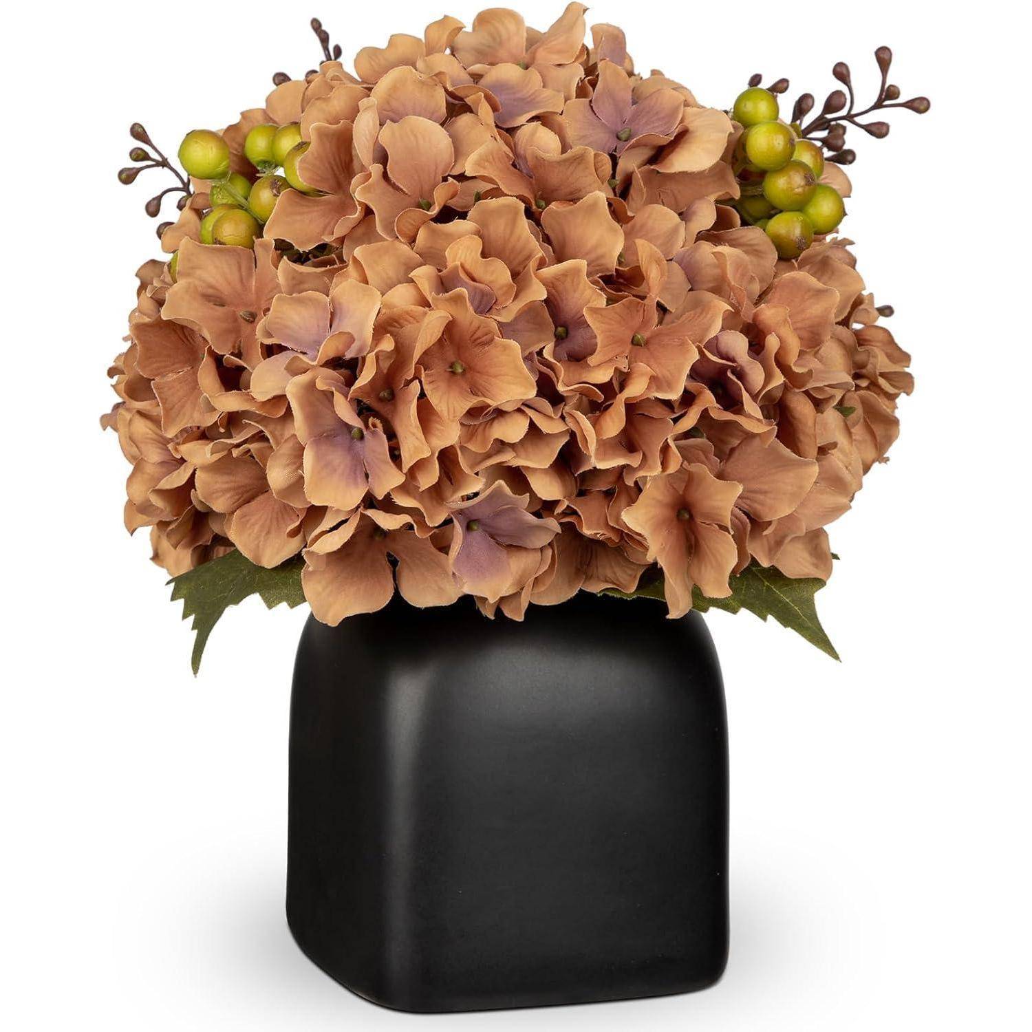 Ein Blumenstrauß aus hellbraunen Hortensien mit grünen Beeren, arrangiert in einer quadratischen schwarzen Vase, der eine elegante und gedämpfte Blumenkomposition bildet.