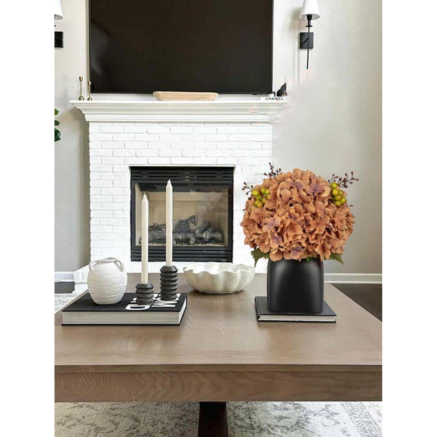 Ein Wohnzimmer mit einem weißen Ziegelkamin, über dem ein großer Fernseher hängt. Auf dem Couchtisch steht eine Vase mit orangefarbenen Blumen und zwei Kerzen.