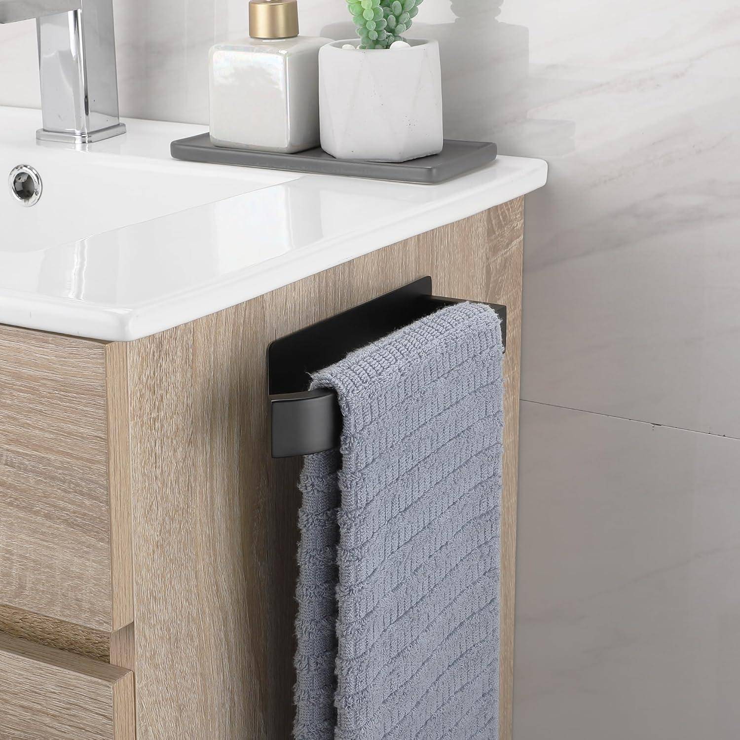 Ein modernes Badezimmerwaschbecken mit einem Unterschrank aus hellem Holz, einem zusammengelegten blau-grauen Handtuch an einem schwarzen Halter und dekorativen Gegenständen auf der Ablage.