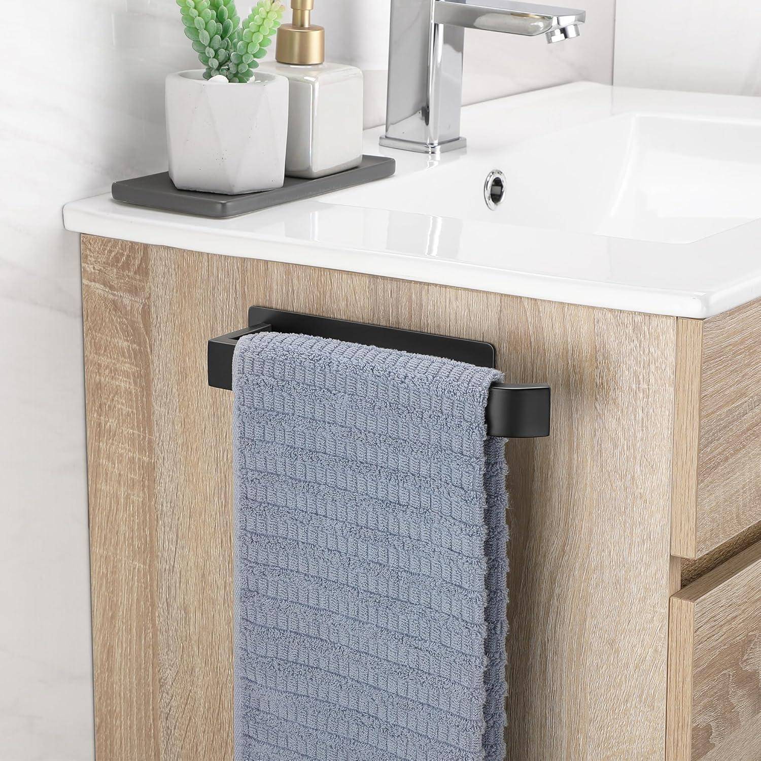 Ein modernes Waschbecken mit einer Chromarmatur, einem Holzschrank und einem grauen Handtuch, das an einer schwarzen Stange hängt. Eine kleine Pflanze schmückt die Theke.