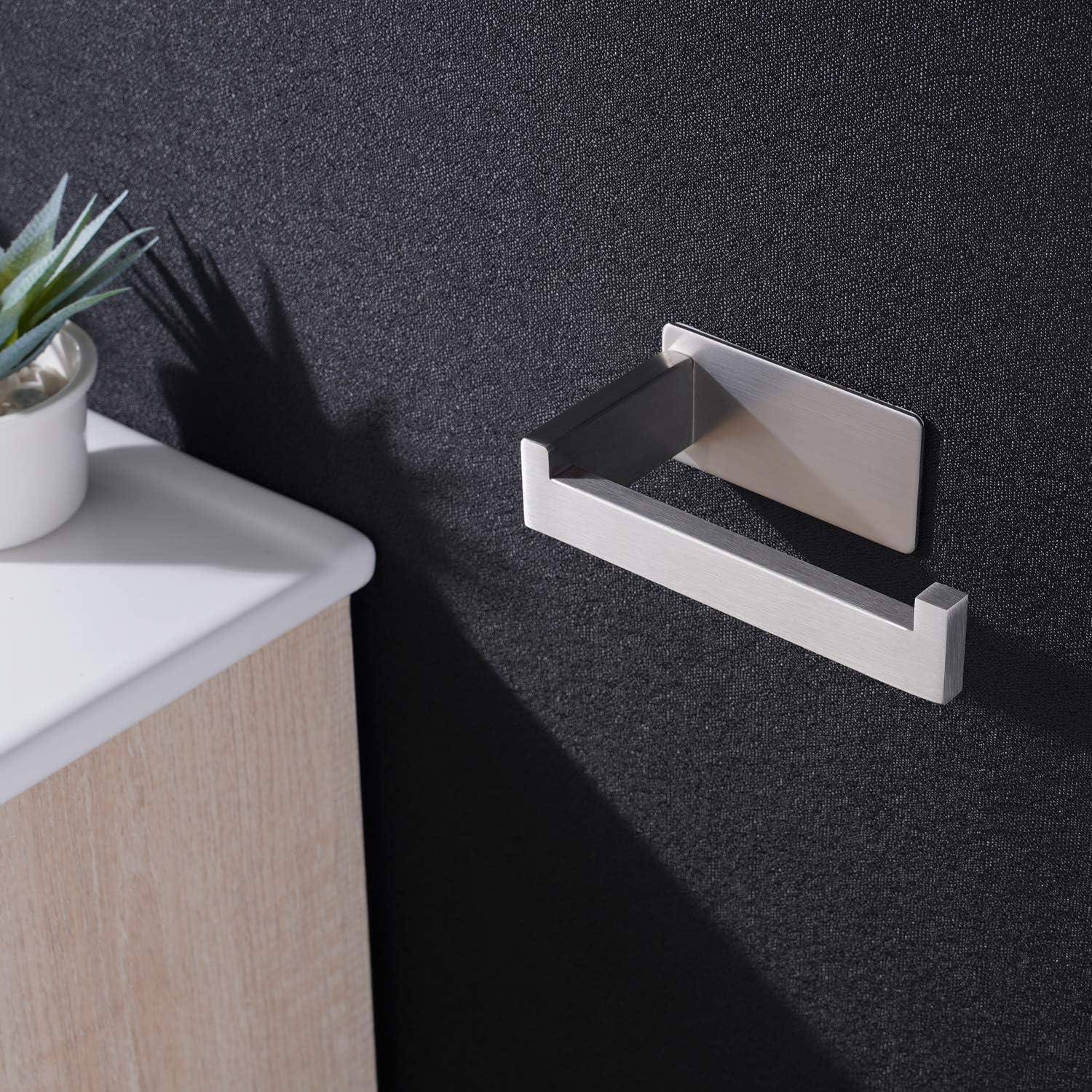 Ein Toilettenpapierhalter aus Metall ist an einer Wand über einem hellen Holzschrank montiert. Eine kleine Pflanze in einem weißen Topf steht auf dem Schrank.