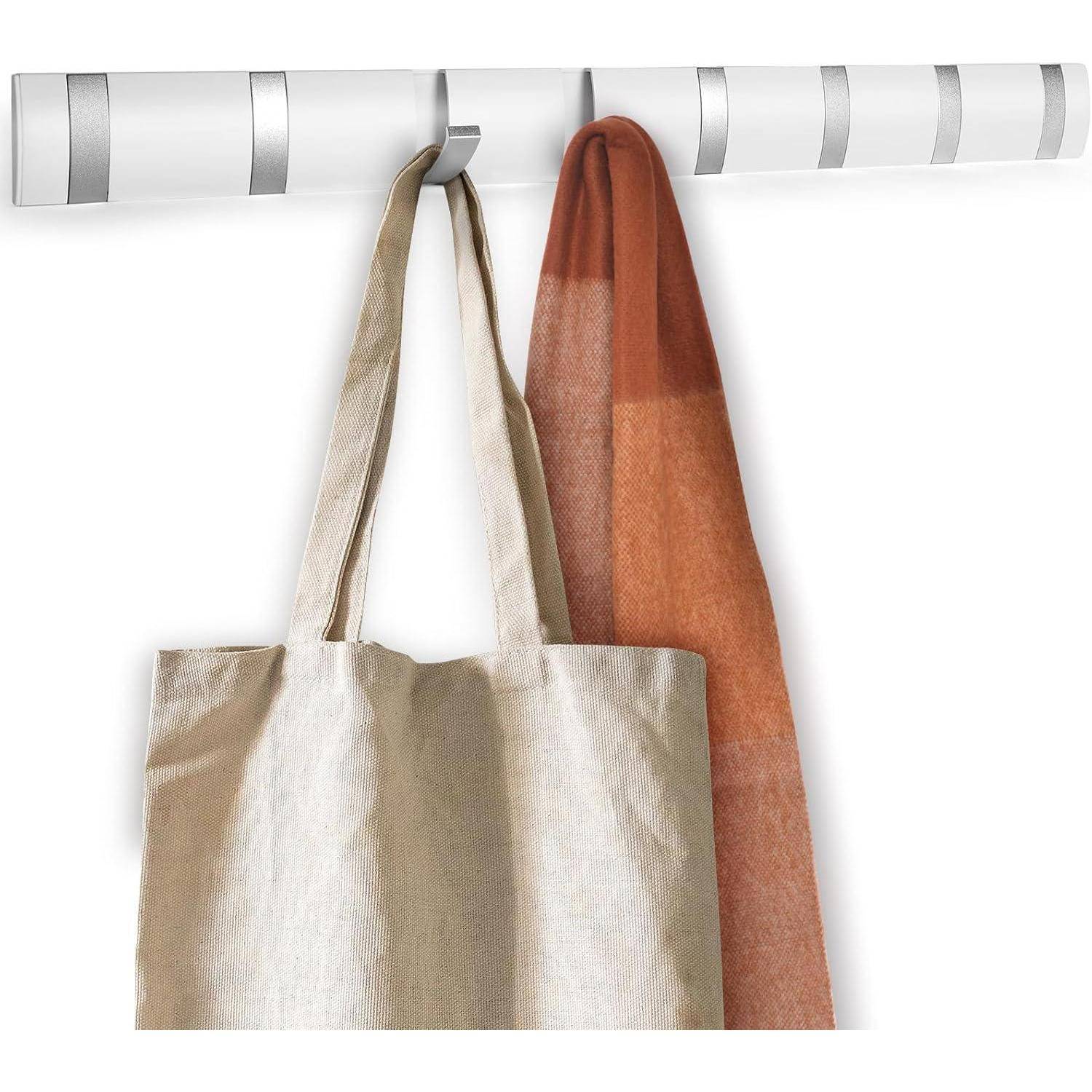Eine beige Tragetasche und ein roter Schal, die an einem modernen, gestreiften Wandhaken hängen.