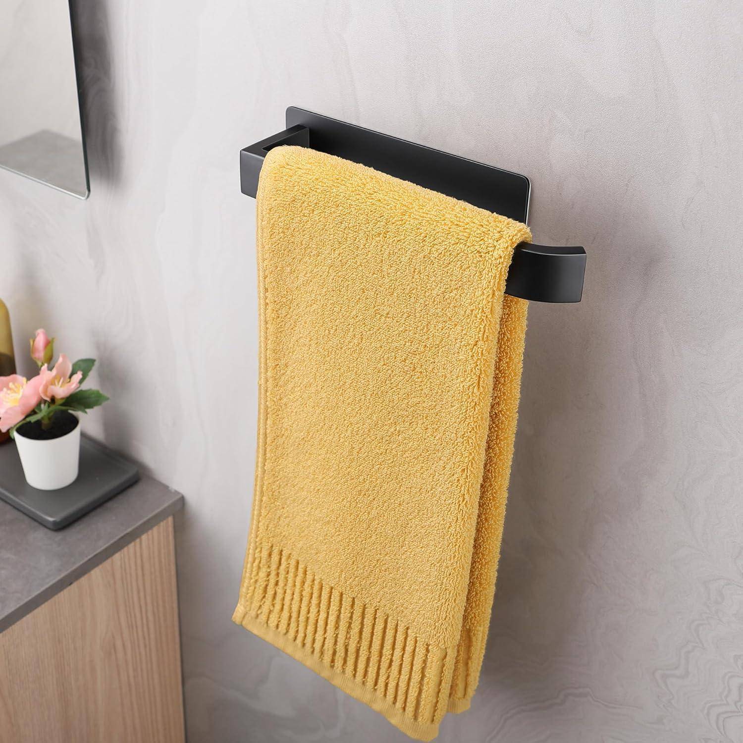 Ein gelbes Handtuch hängt ordentlich an einem schwarzen Handtuchhalter vor einer grauen Wand; eine kleine Zimmerpflanze steht auf der danebenliegenden Theke.