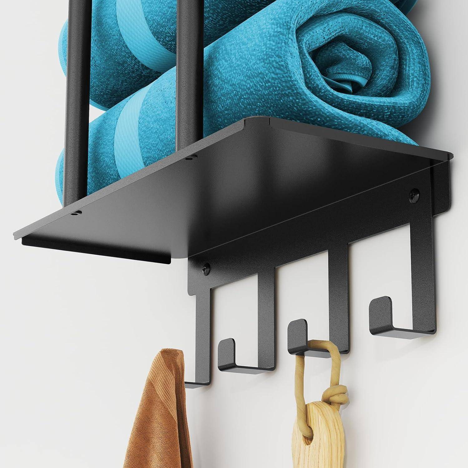 Ein an der Wand befestigtes schwarzes Metallregal mit zwei aufgerollten blauen Handtüchern oben, darunter Haken, an denen eine braune Ledertasche und ein Holzbügel hängen.