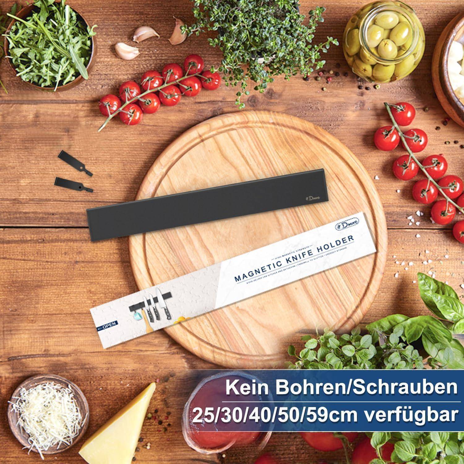 Ein Set von Küchenutensilien bestehend aus einem runden Holzschneidebrett, Tomaten, Kräutern und einem verpackten magnetischen Messerhalter auf einer Holzoberfläche.