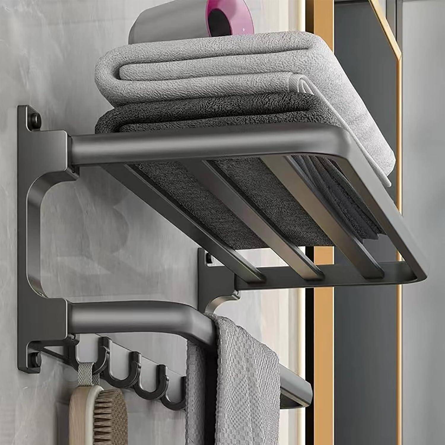 Ein Metallregal im Badezimmer mit gefalteten grauen Handtüchern, einer rosa Toilettenpapierrolle oben und Haken darunter, an denen ein graues Handtuch und eine Bürste hängen.