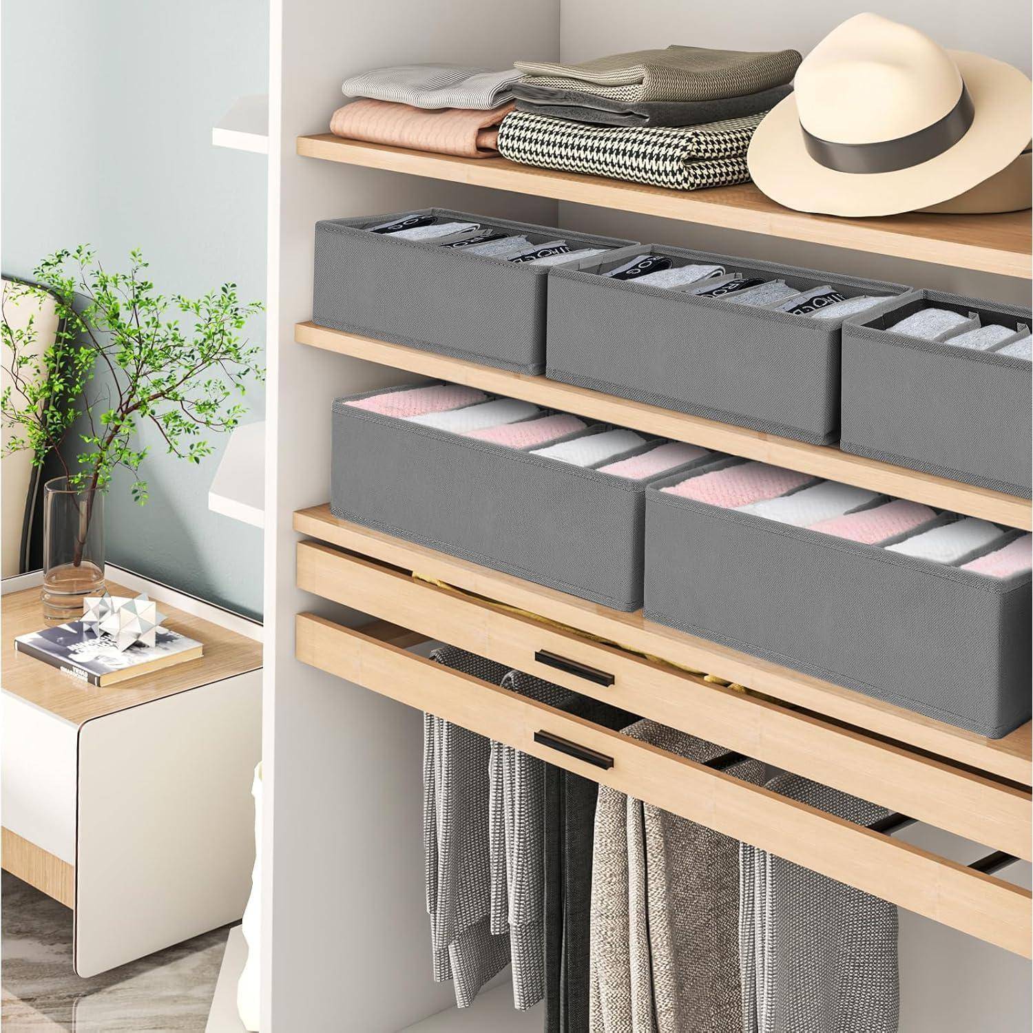 Geöffneter Kleiderschrank mit organisierten Regalen, ausgestattet mit zusammenlegbaren Aufbewahrungsboxen, die für verschiedene Gegenstände beschriftet sind. Hüte und zusammengelegte Kleidungsstücke auf dem obersten Regal.