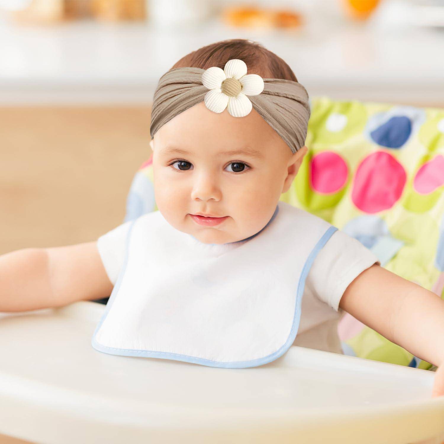 Ein Baby mit einer grauen Stirnband mit einer Blume sitzt in einem Hochstuhl und lächelt, mit einem Tupfenstoff-Hintergrund.
