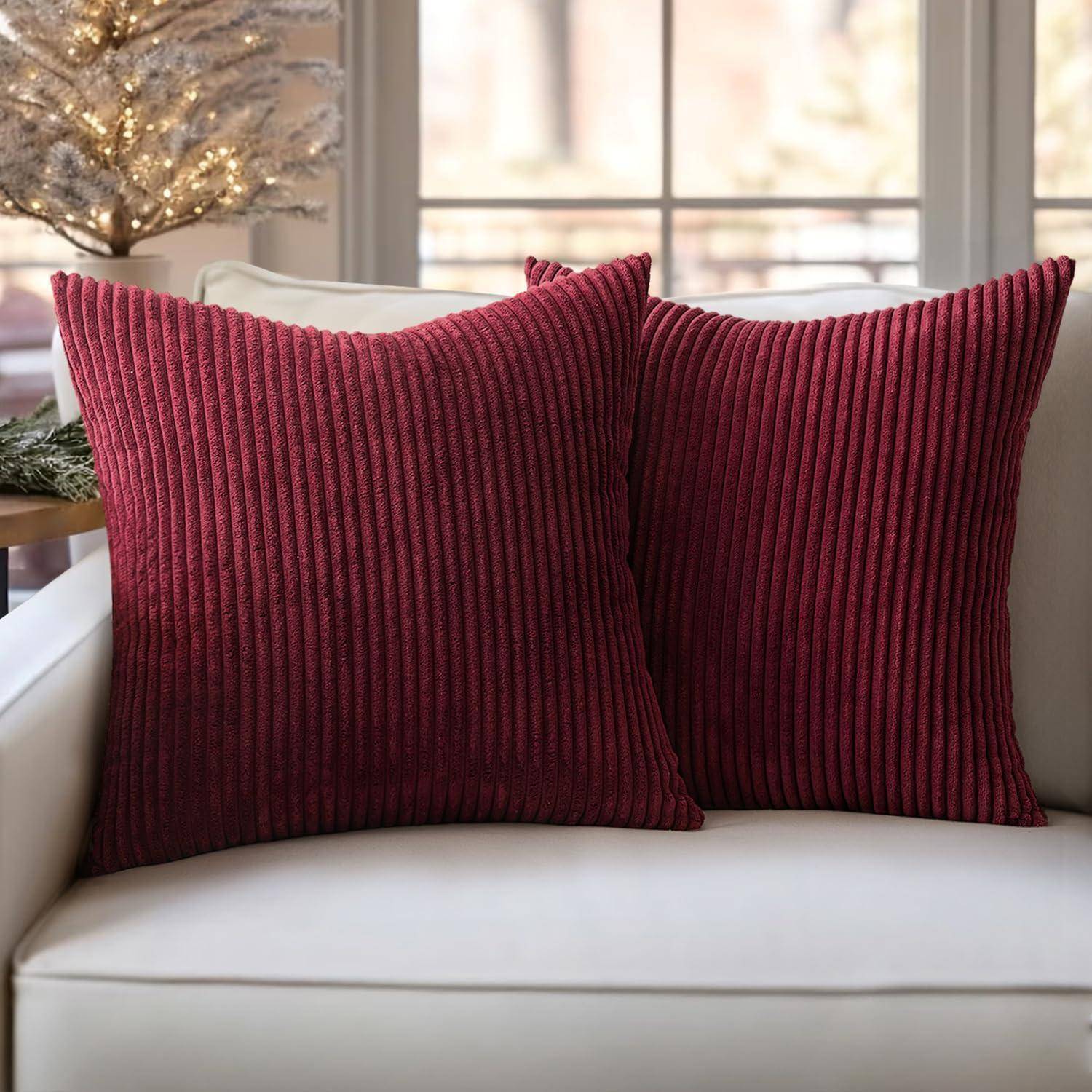 Rote, gerippte Zierkissen auf einem weißen Sofa, mit einem geschmückten, beleuchteten Weihnachtsbaum im Hintergrund.