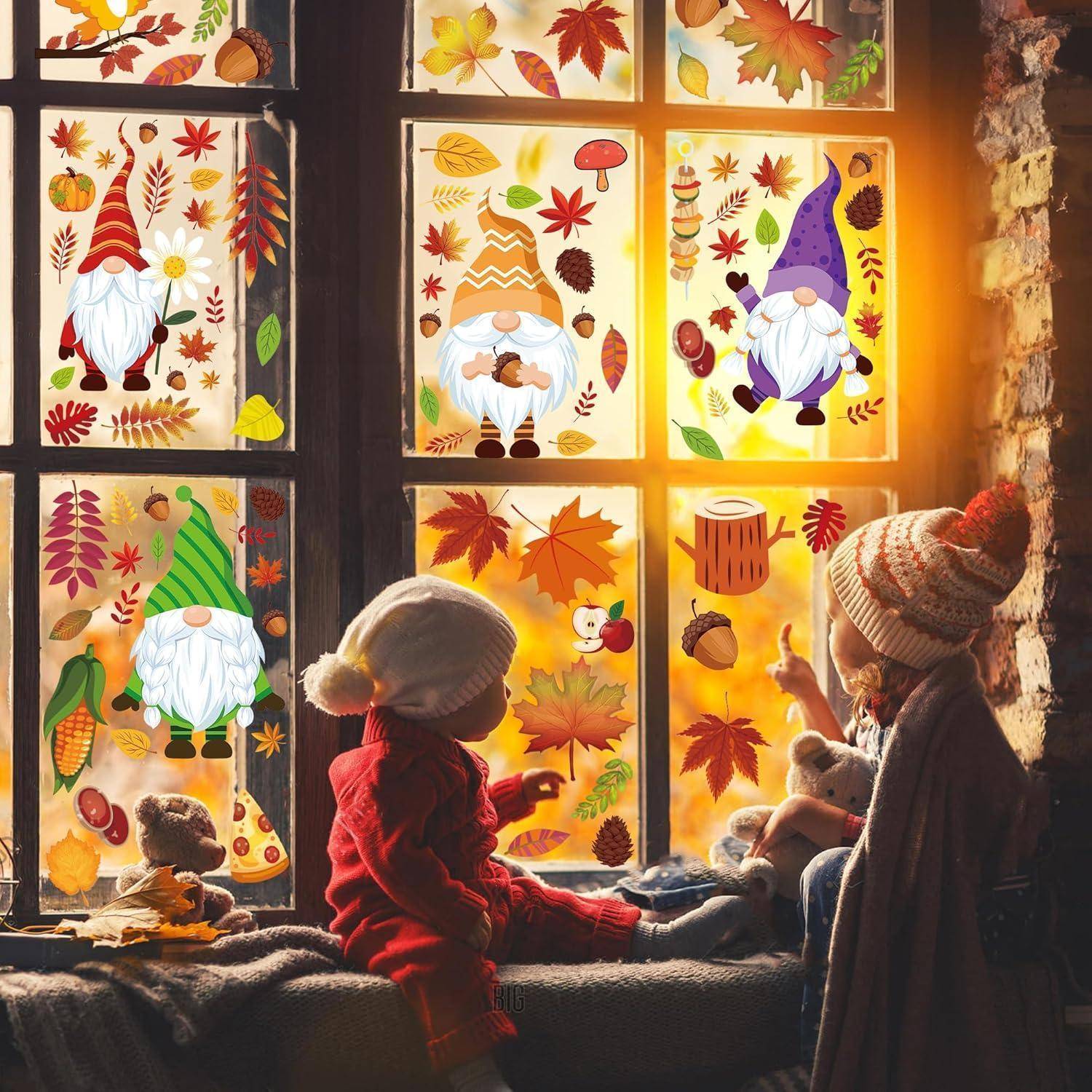 Zwei Kinder in warmer Kleidung sitzen an einem Fenster, das mit herbstlichen Aufklebern geschmückt ist, auf denen Gnome, Blätter und Eicheln zu sehen sind. Warmes Licht durchflutet den Raum.