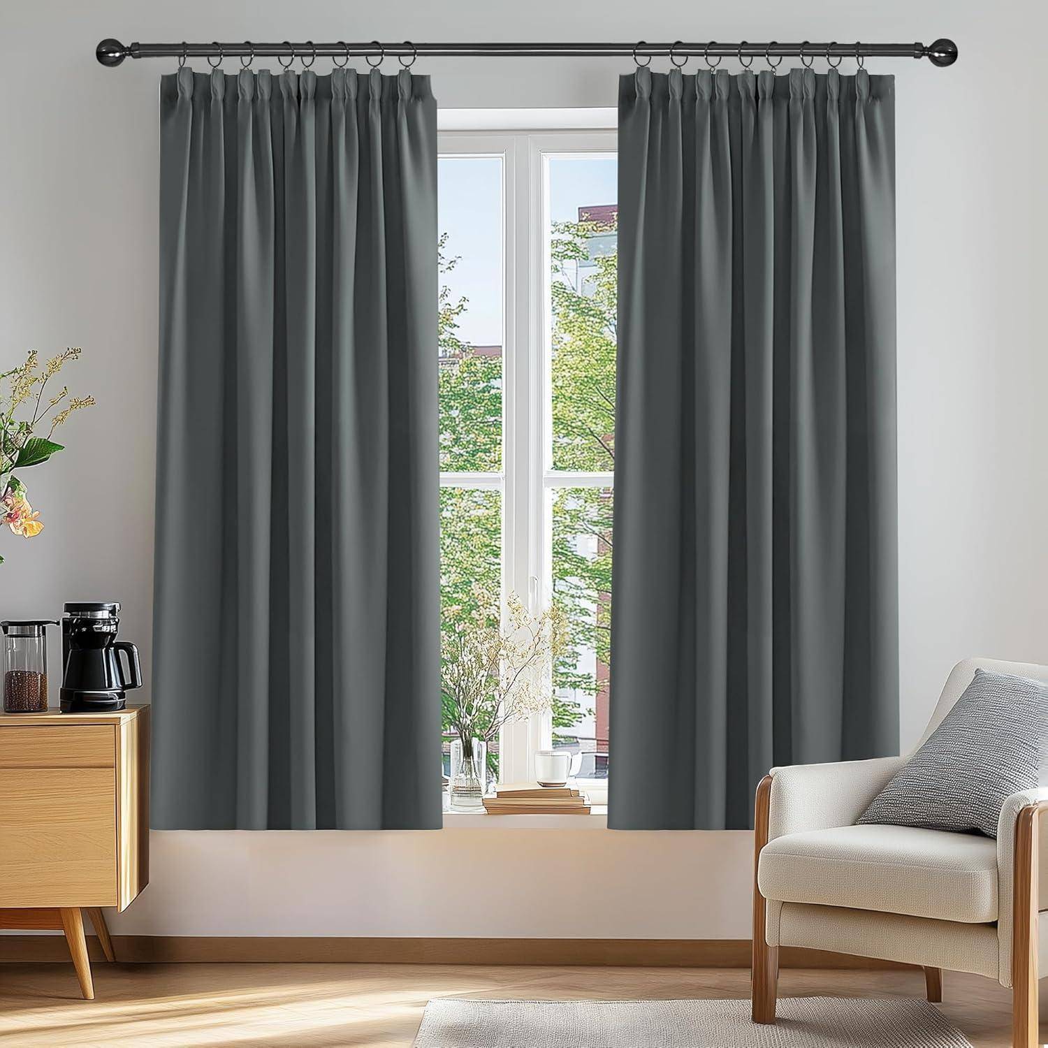 Ein gemütlicher Wohnbereich mit zwei grauen Vorhängen, die ein Fenster umrahmen. Ein einzelner Sessel und ein Holzschrank mit einer Kaffeemaschine sind zu sehen.