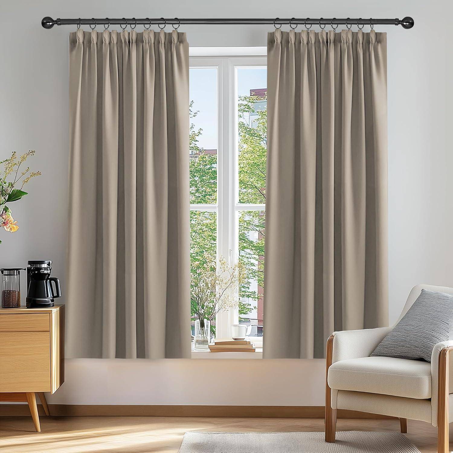 Wohnzimmer mit beigen Vorhängen vor einem großen Fenster, einem hellen Sessel und einem Holzschrank, auf dem eine Kaffeemaschine steht. Draußen sind Bäume zu sehen.