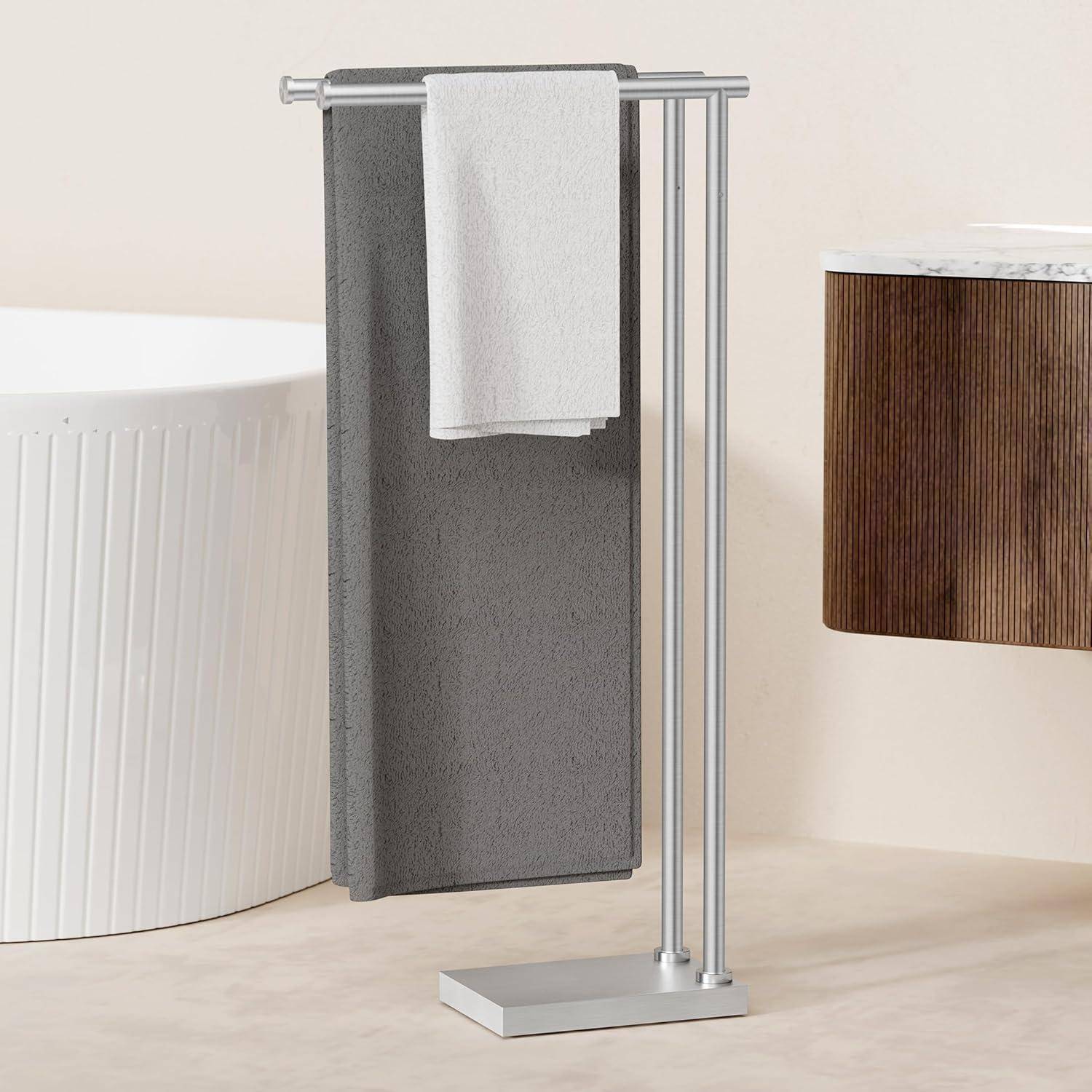 Ein modernes freistehendes Handtuchgestell mit einem grauen Handtuch und einem kleineren weißen Handtuch hängt neben einer Badewanne in einem minimalistischen Badezimmerambiente.