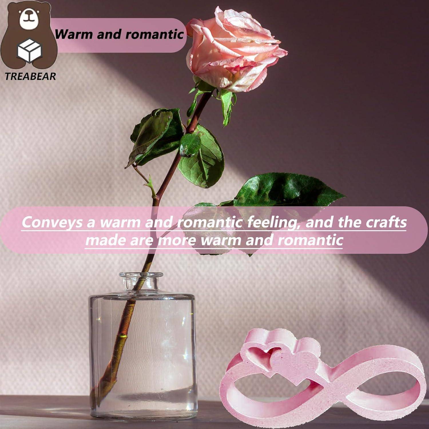 Eine rosa Rose in einer Vase auf einem Tisch bei sanftem Licht. Ein rosa Unendlichkeitssymbol mit Herzen liegt daneben. Text lautet: „Warm und romantisch.