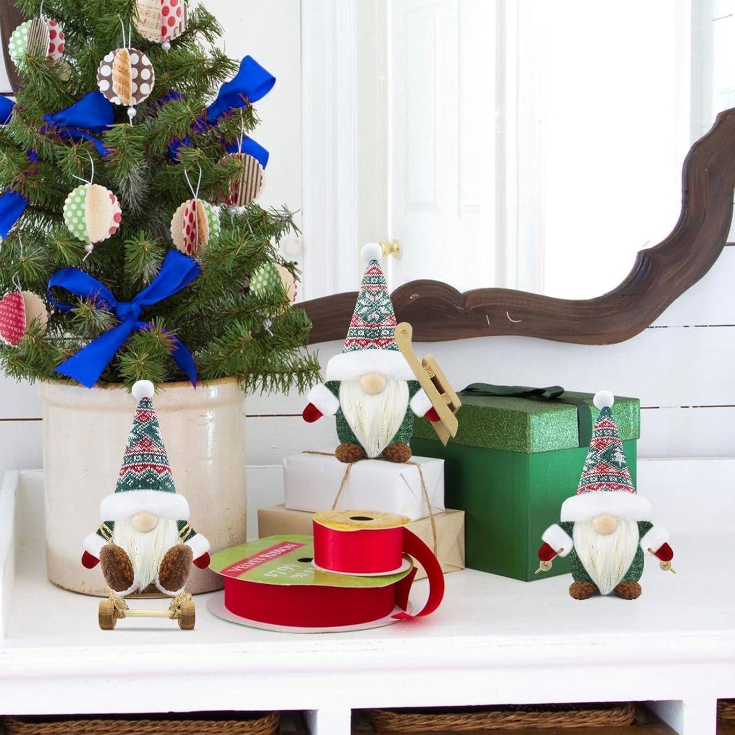 Ein kleiner Weihnachtsbaum mit bunten Christbaumkugeln und blauen Bändern auf einem Tisch mit Wichtel-Dekorationen, Geschenkboxen und Bandspulen.