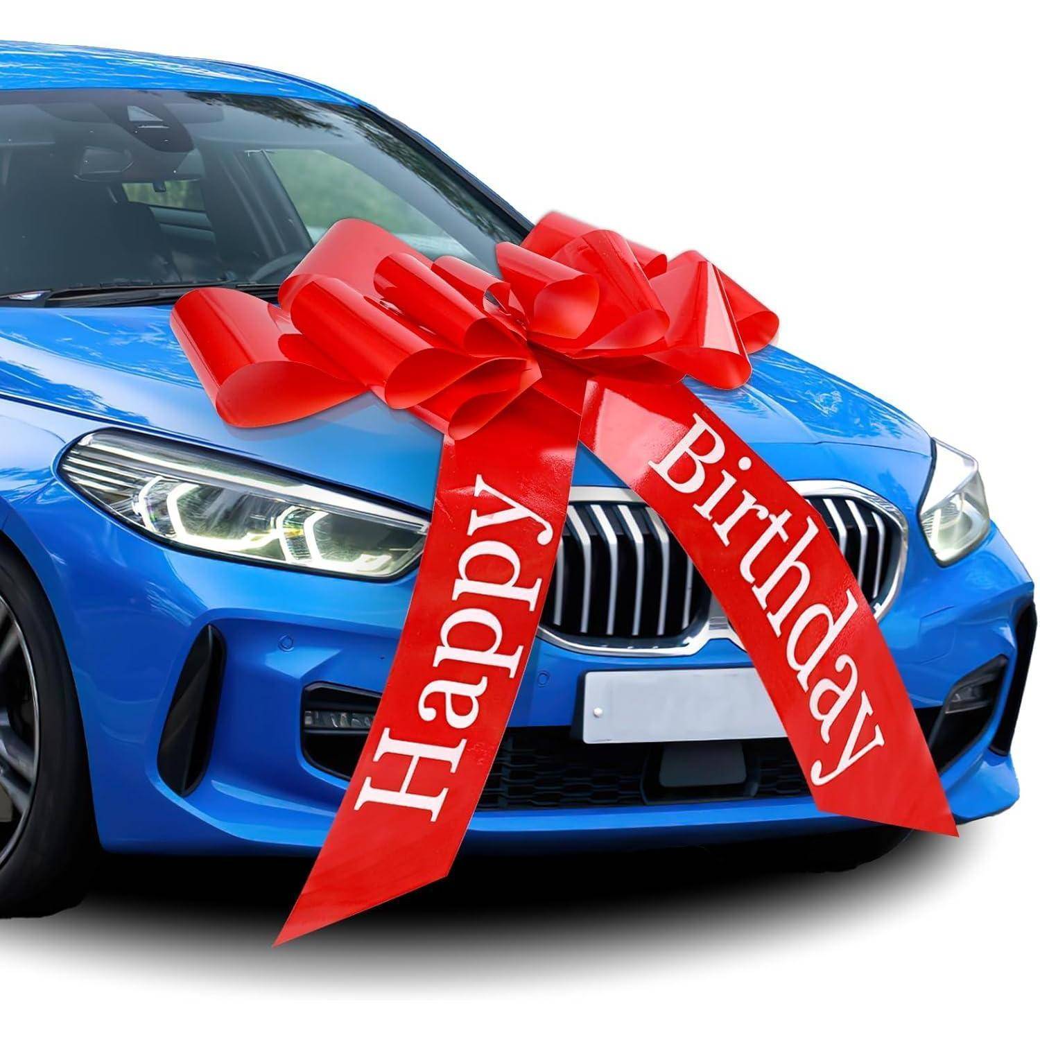 Ein blauer Wagen, geschmückt mit einer großen roten Schleife auf der Motorhaube, versehen mit dem Text ‚Alles Gute zum Geburtstag', was darauf hindeutet, dass es sich um ein Geburtstagsgeschenk handelt.