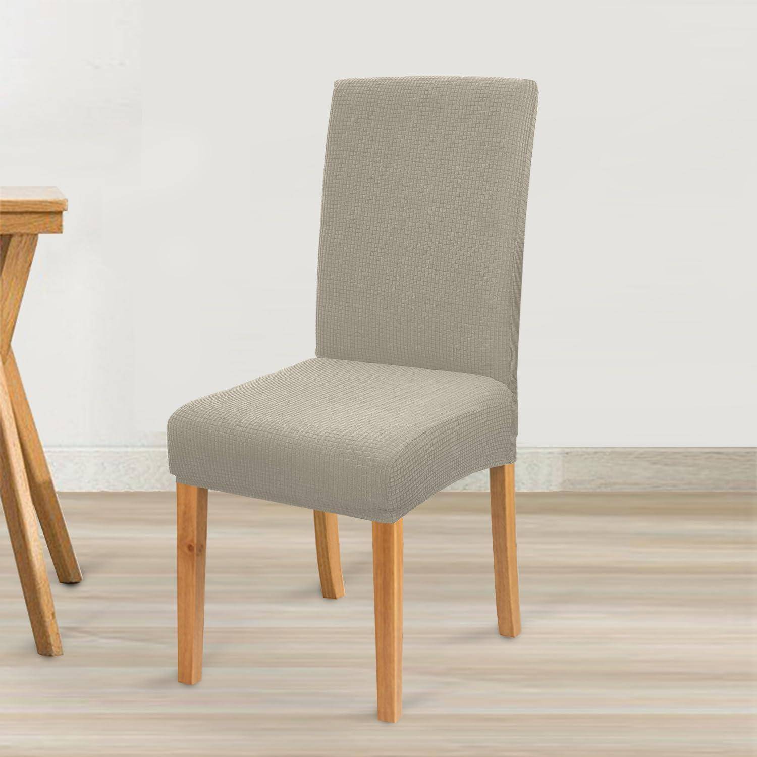 Ein hellgrau gepolsterter Stuhl mit Holzbeinen steht auf einem hellen Holzboden neben einem kleinen Holztisch vor einer schlichten Wand.