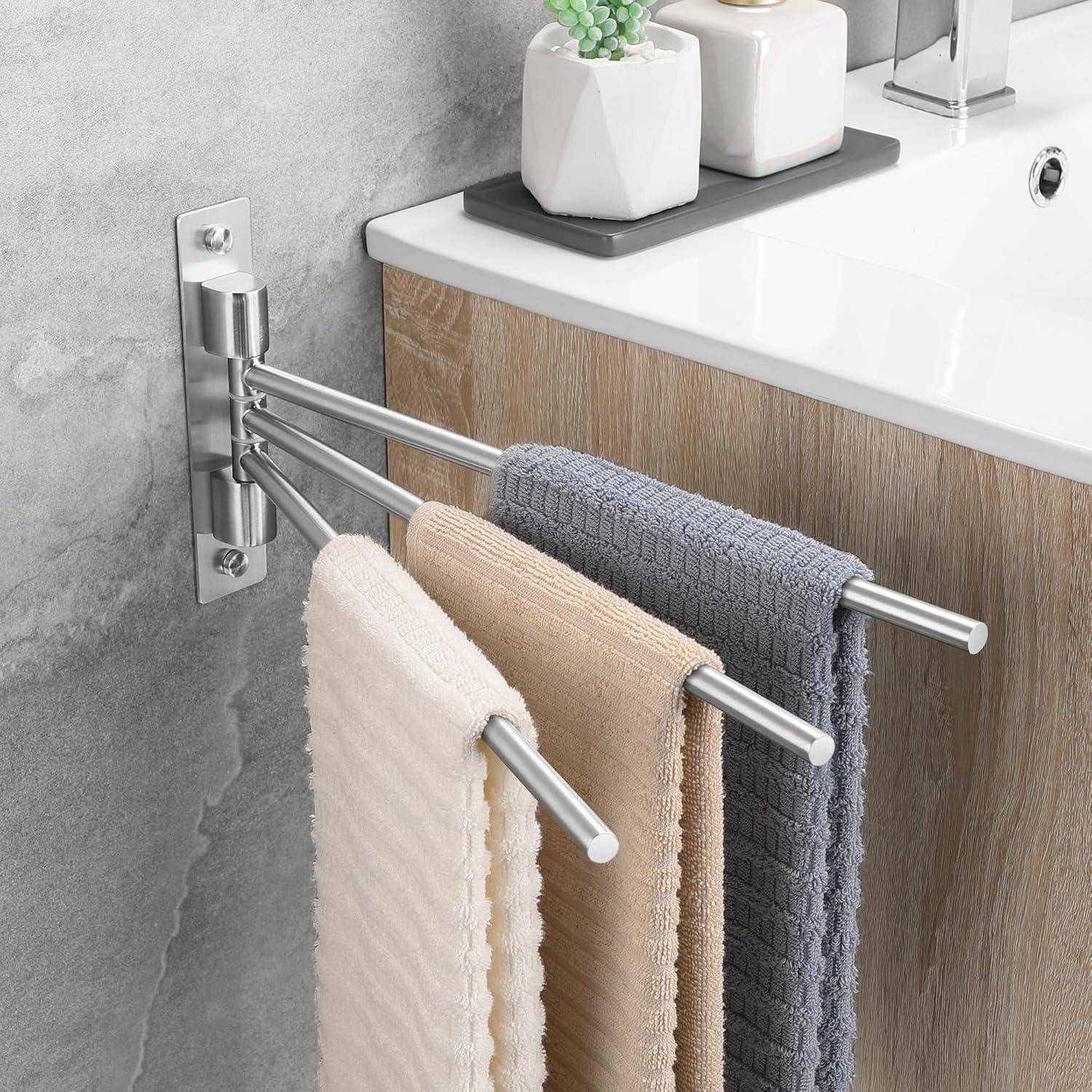 Eine Badezimmerszene, die drei Handtücher in Beige, Grau und Weiß zeigt, die an einer wandmontiertem Halterung neben einem Waschbecken hängen. Eine Pflanze und Körperpflegeprodukte stehen auf der Ablage.